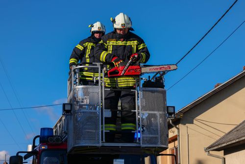 Free Firefighters in action on a ladder truck, using a chainsaw for rescue operations under a clear blue sky. Stock Photo