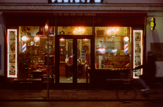 Warmly lit barbershop entrance in Copenhagen at nighttime, vintage decor and urban setting.