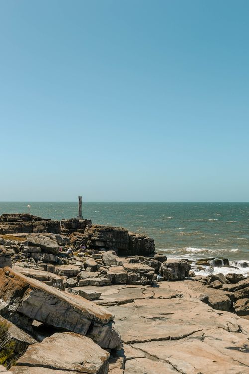 Free Explore the rocky shoreline of Mar del Plata, Argentina, under clear summer skies. Stock Photo