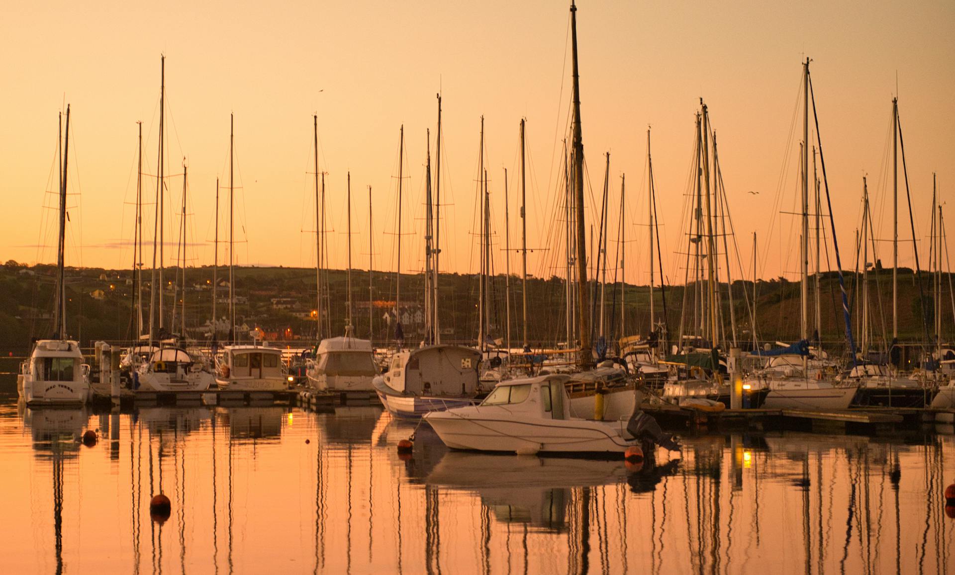 A peaceful view of sailboats in Kinsale Harbor at sunset, showcasing serene reflections and warm hues.