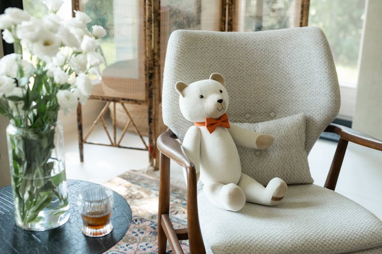 White Teddy Bear Sitting In A Chair Next To The Table With A Glass Of Whiskey