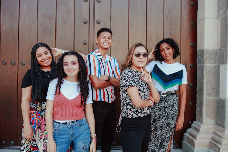 Photo Of Young People Smiling And Posing In Front Of Entrance Door To A Building