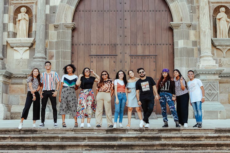 Photo Of Young People Smiling And Posing In Front Of Entrance Door To A Building