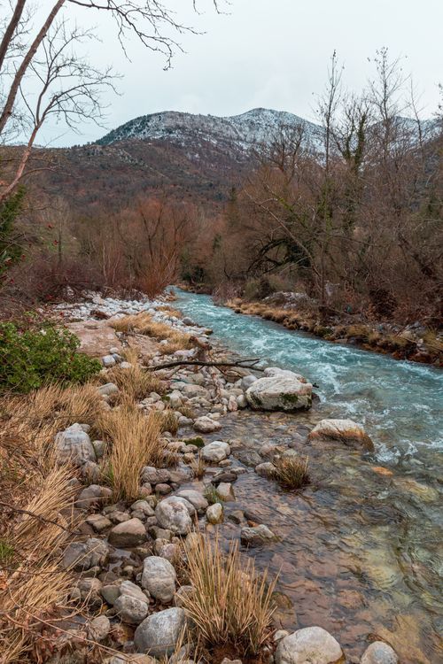 Free A picturesque mountain stream flowing through a serene winter landscape with stones and trees. Stock Photo