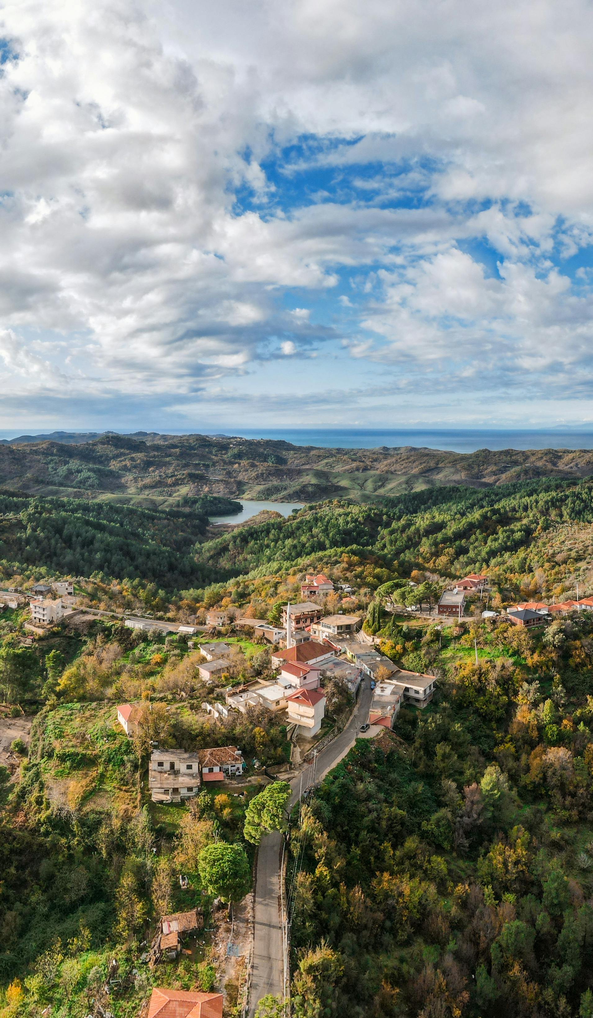 Drone captures winding road through vibrant mountain village landscape with lush forests.