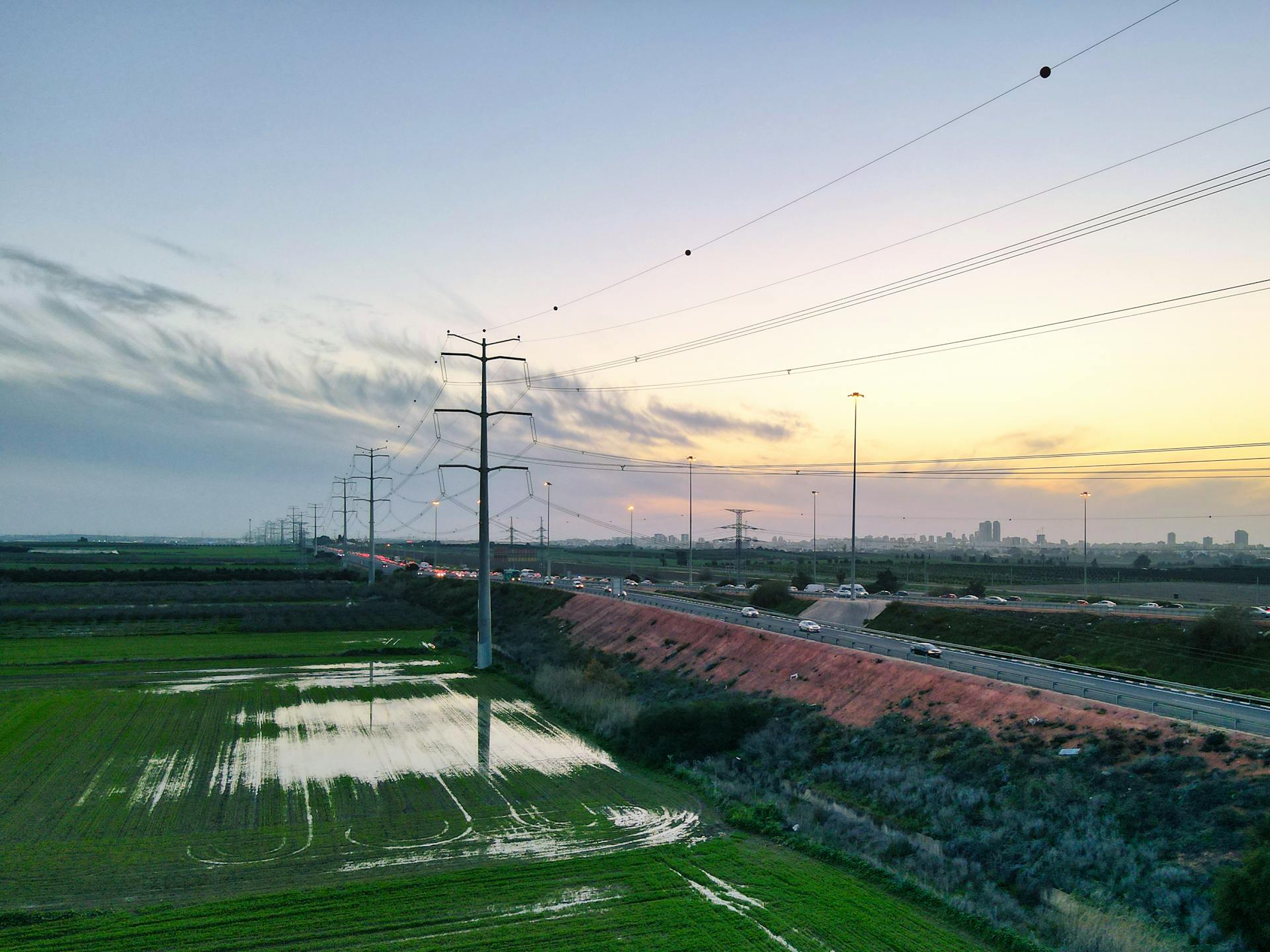 Stunning aerial view of transmission towers over fields near a highway at sunset in Gan HaDarom, Israel.