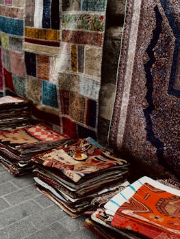 Vibrant assortment of handmade carpets and fabrics stacked in a traditional market setting.