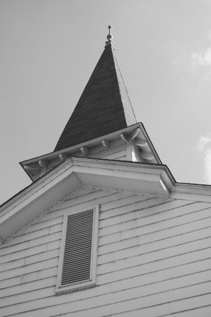 A low-angle black and white photo of a colonial church steeple against a clear sky.