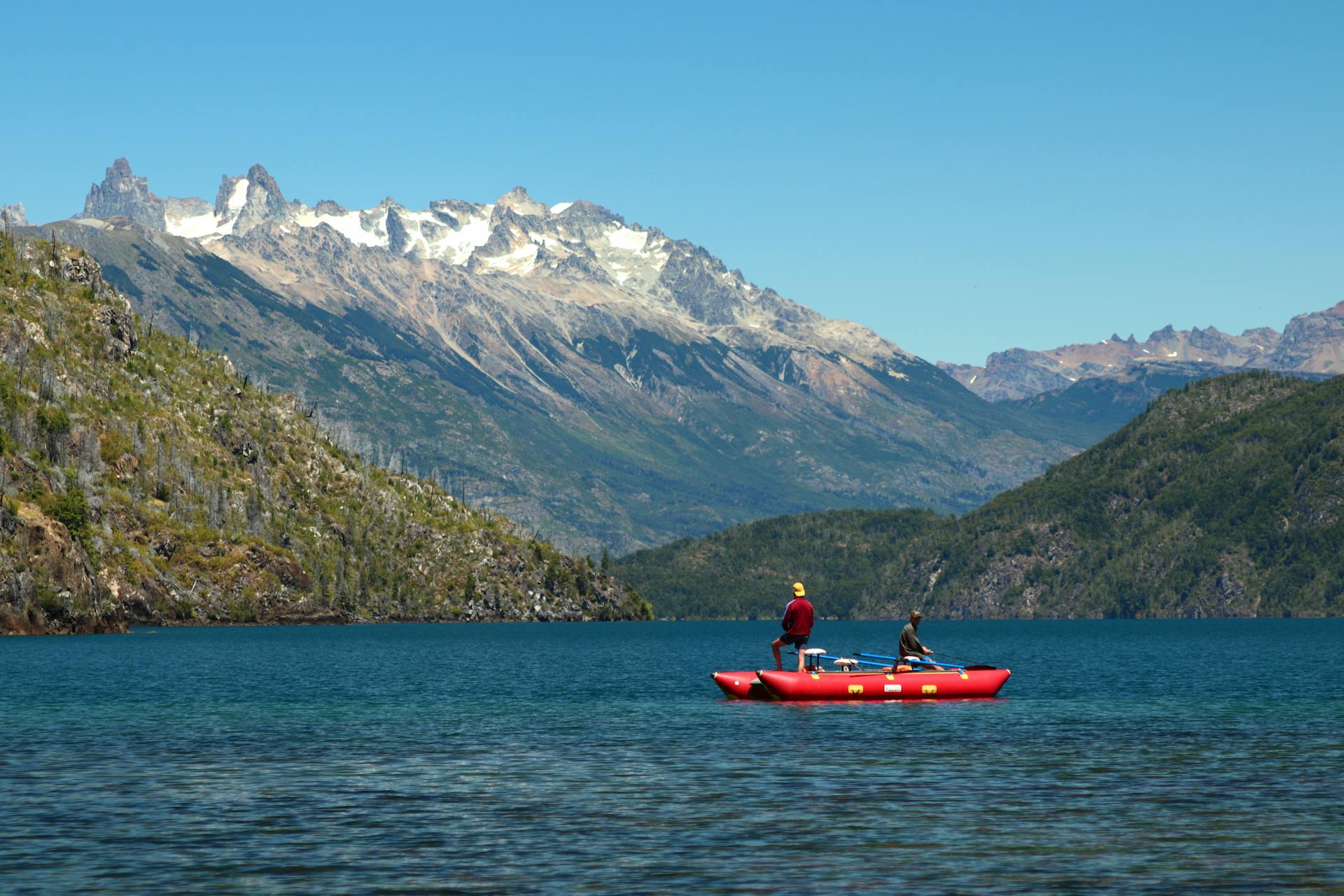 Two people on a red catamaran enjoying scenic mountain lake views for leisurely adventure.