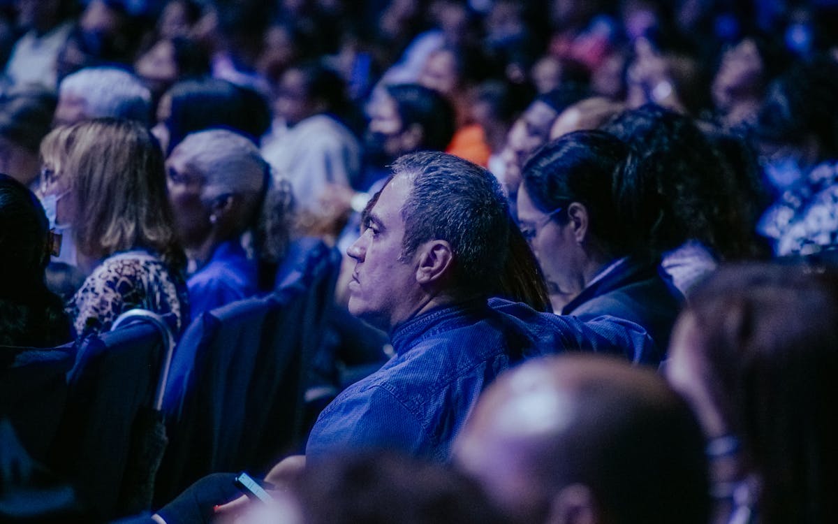 A large, diverse audience attentively listens during an indoor event.