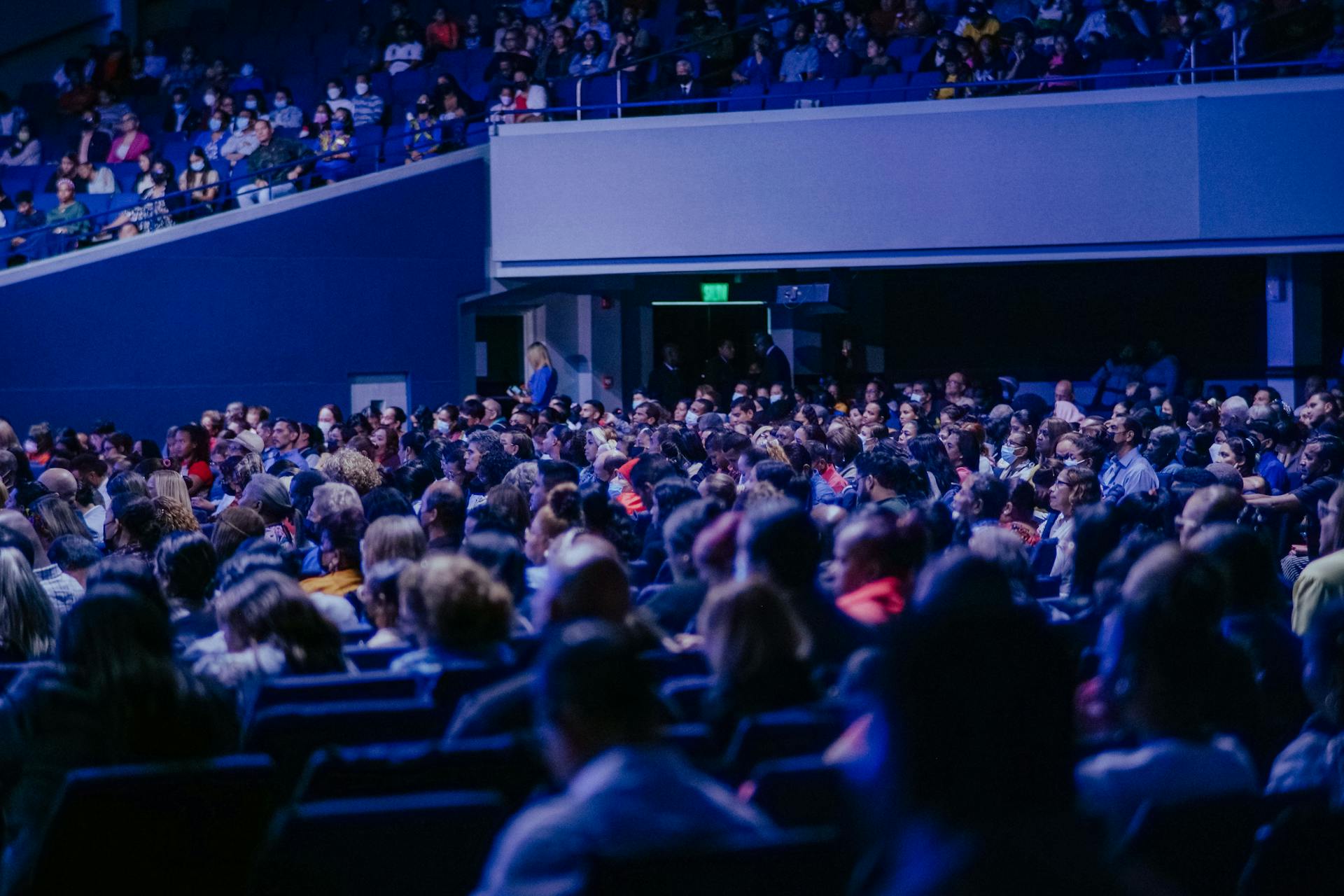 A crowded conference hall with diverse audience attentively listening to a speaker.