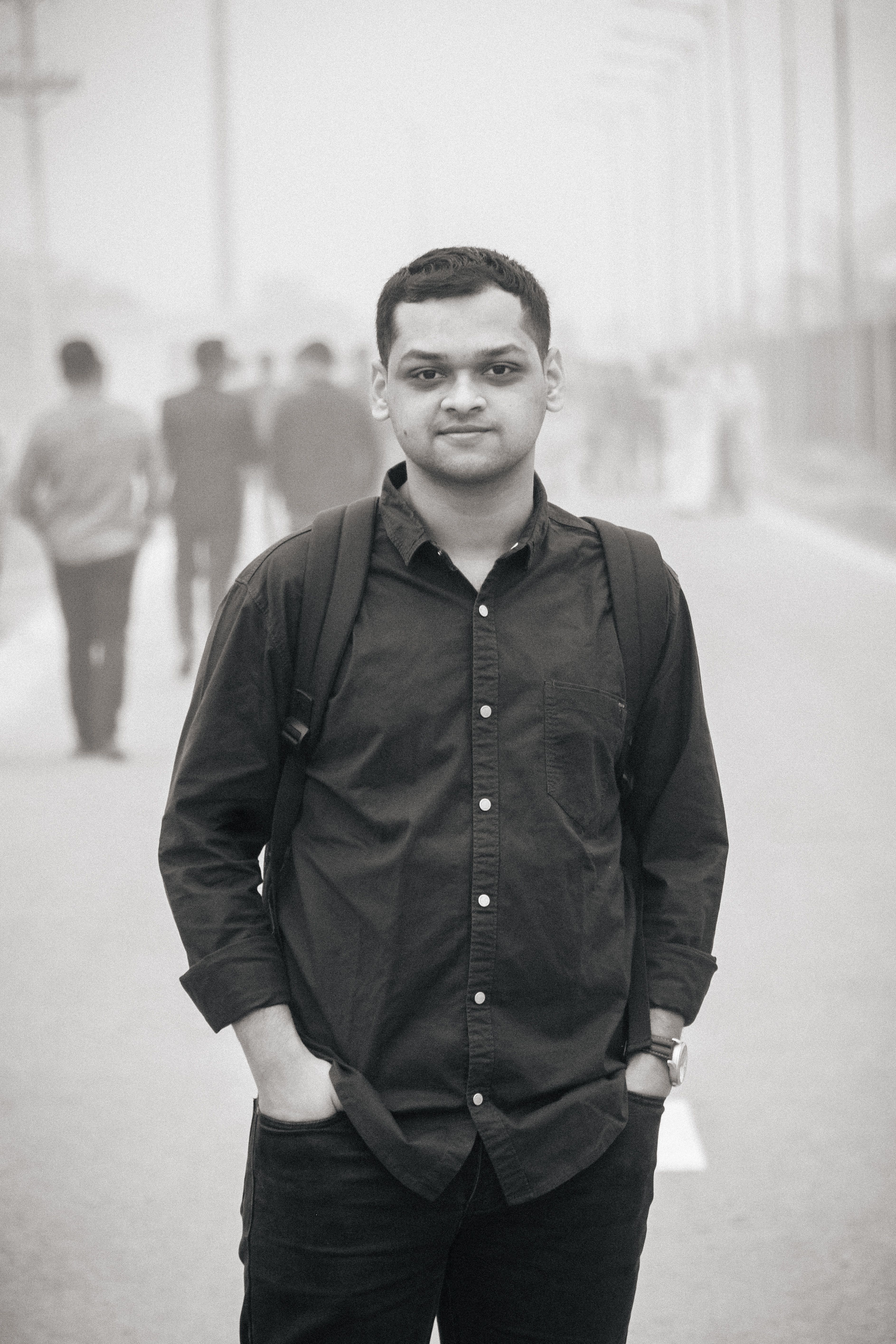 A young adult man in black attire poses confidently on a foggy street in Dhaka.