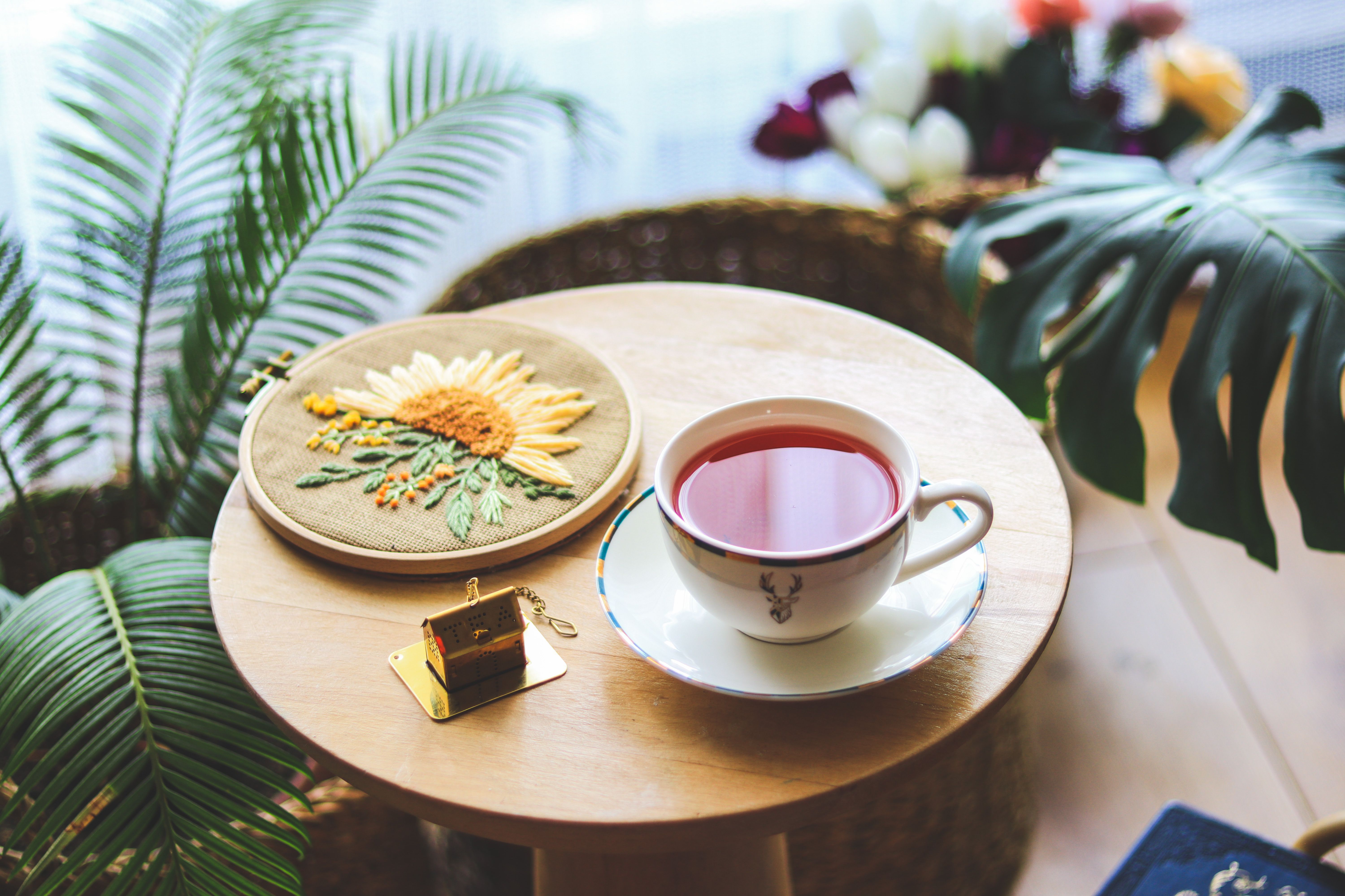 Warm setting with tea and floral embroidery, surrounded by lush plants.