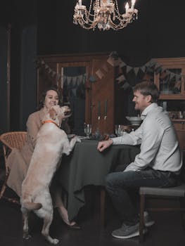 A couple enjoys a cozy dinner indoors with their dog in a warmly lit room.