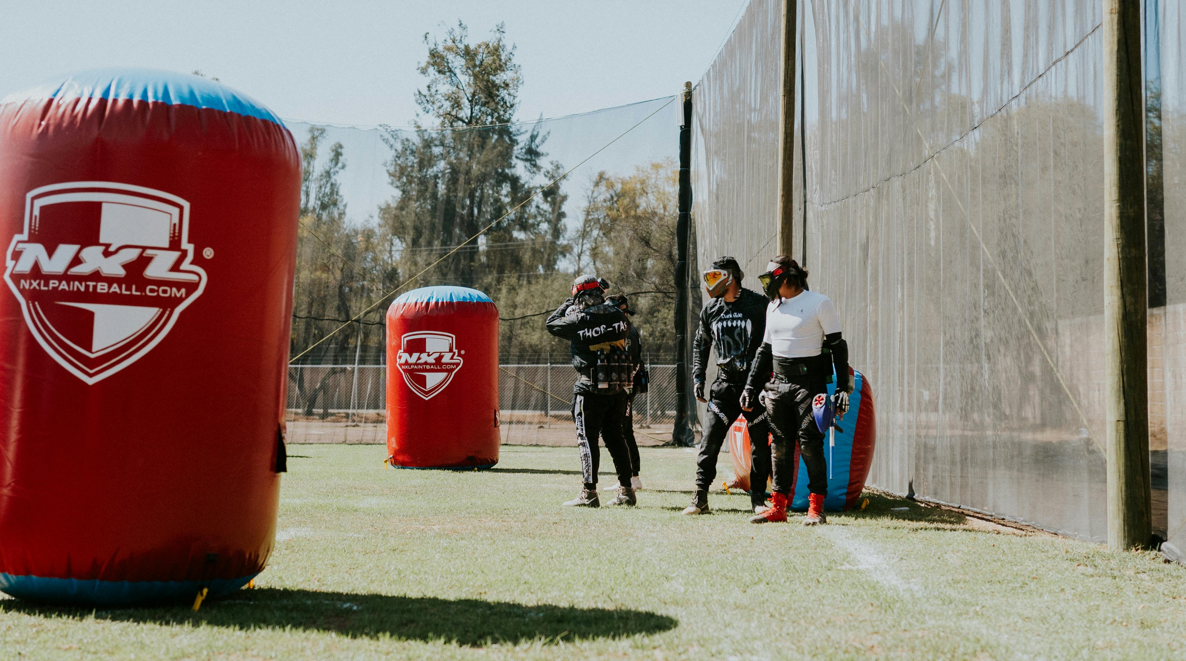 A group of people in protective gear playing paintball on an outdoor field with inflatable barriers. Prescription Goggle Inserts - A group of people in protective gear playing paintball on an outdoor field with inflatable barriers.