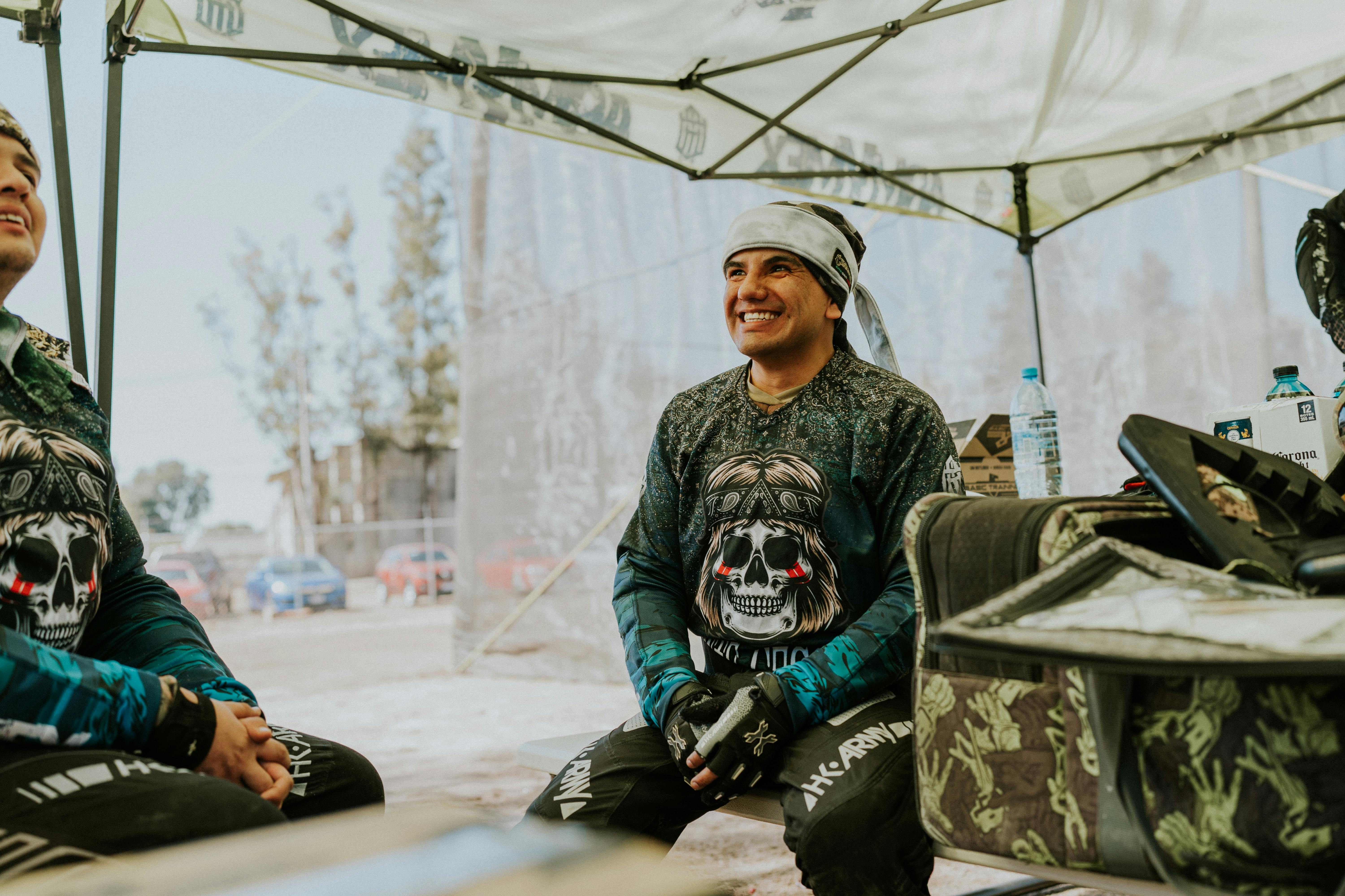 Friends enjoying a fun paintball day outdoors, sitting and smiling under a tent. Prescription Goggle Inserts - Friends enjoying a fun paintball day outdoors, sitting and smiling under a tent.