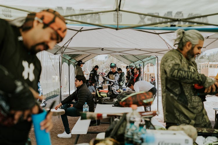 Group Of Men Sitting Under A Tent And Preparing For A Paintball Fight 