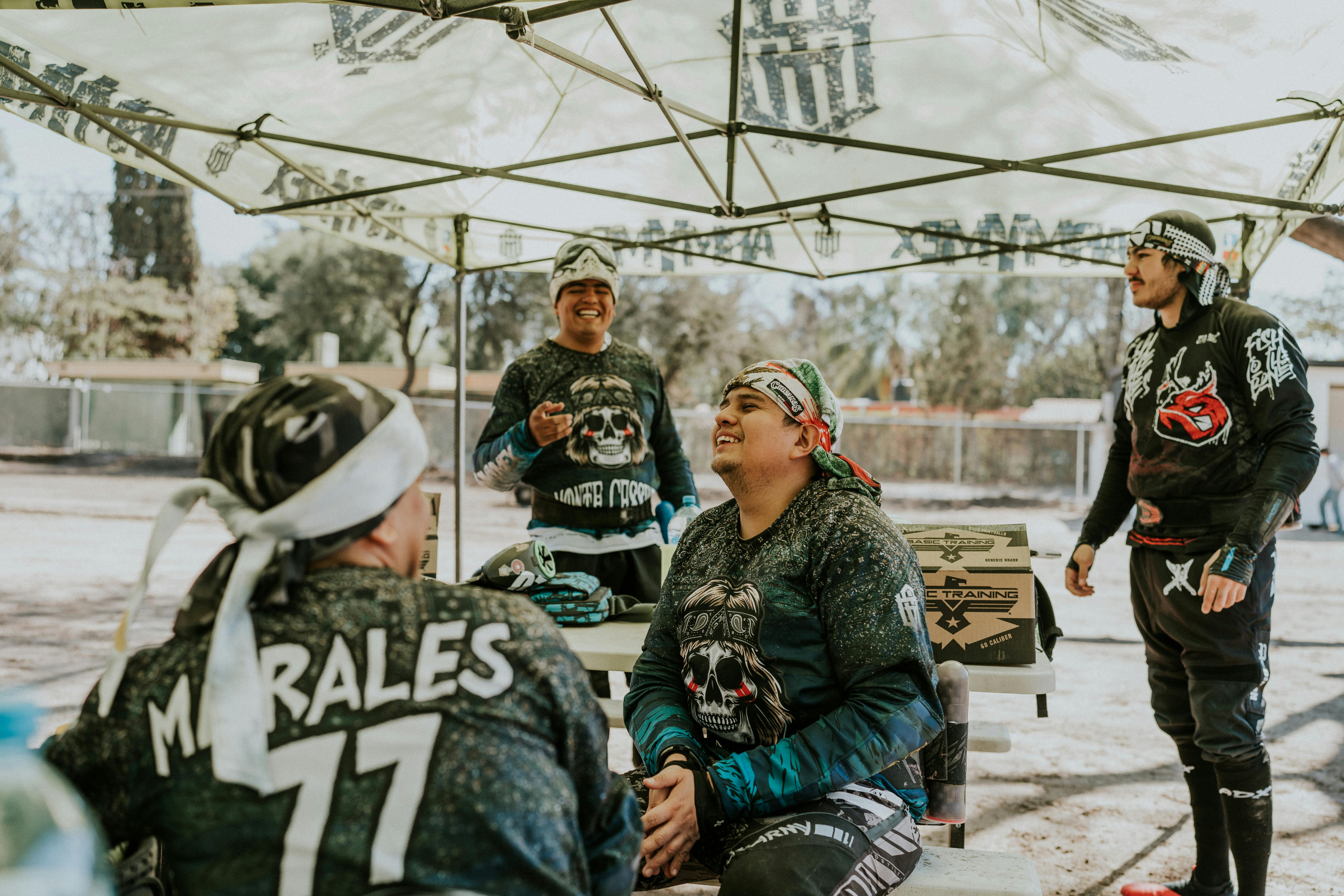 Eine Gruppe Paintballspieler entspannt sich nach einem Spiel unter einem Zelt. Lockere und lebhafte Atmosphäre im Freien. Prescription Goggle Inserts - A group of paintball players relax under a tent after a game. Casual and lively outdoor atmosphere.