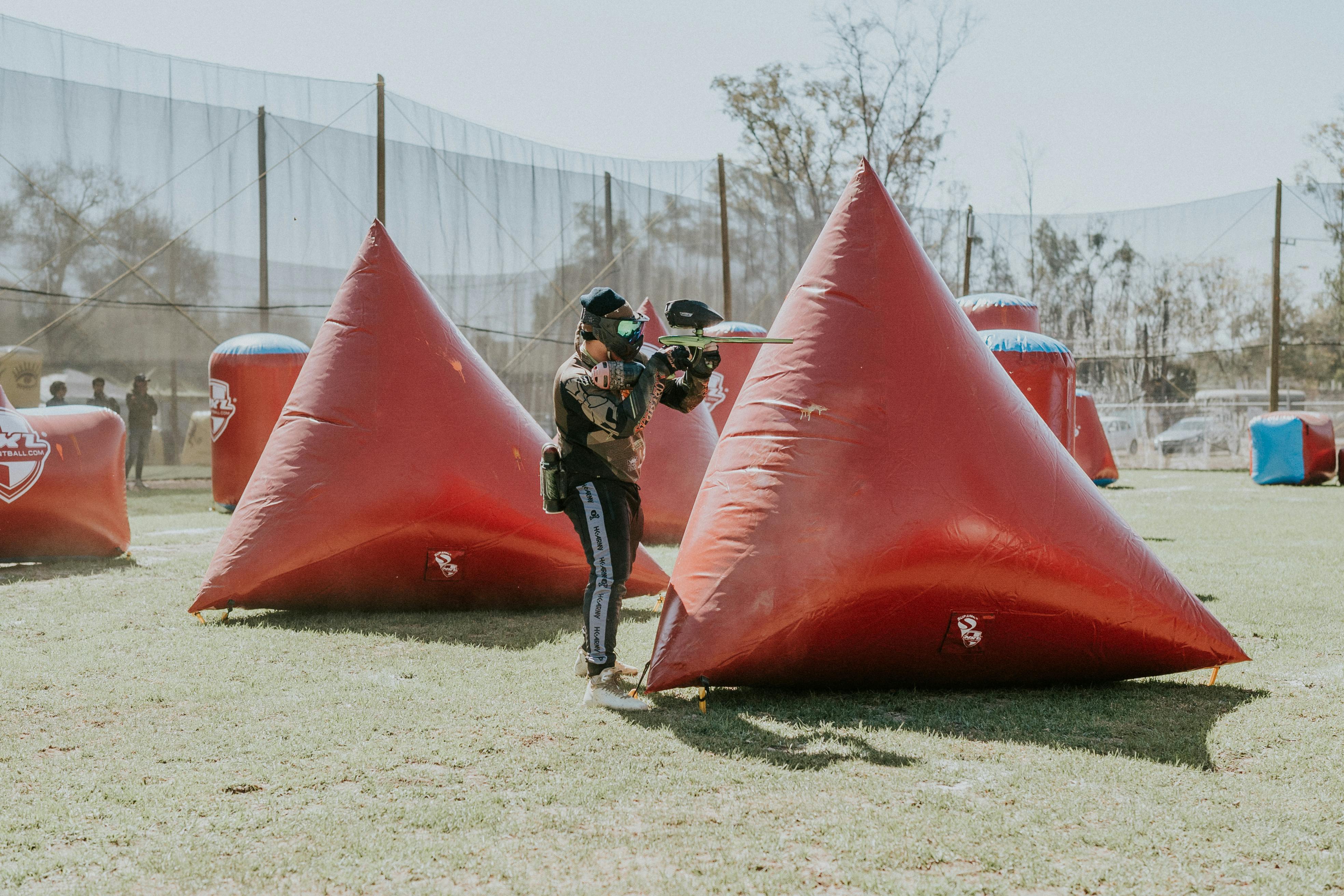Des joueurs de paintball s'adonnent à un jeu en plein air entouré de bunkers gonflables par une journée ensoleillée. Prescription Goggle Inserts - Paintball players engaging in an outdoor game surrounded by inflatable bunkers on a sunny day.