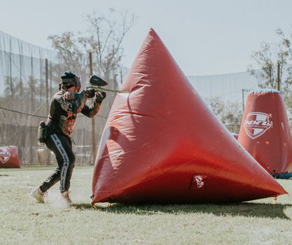 Player engages in a paintball game using vibrant inflatable covers on a sunny day.