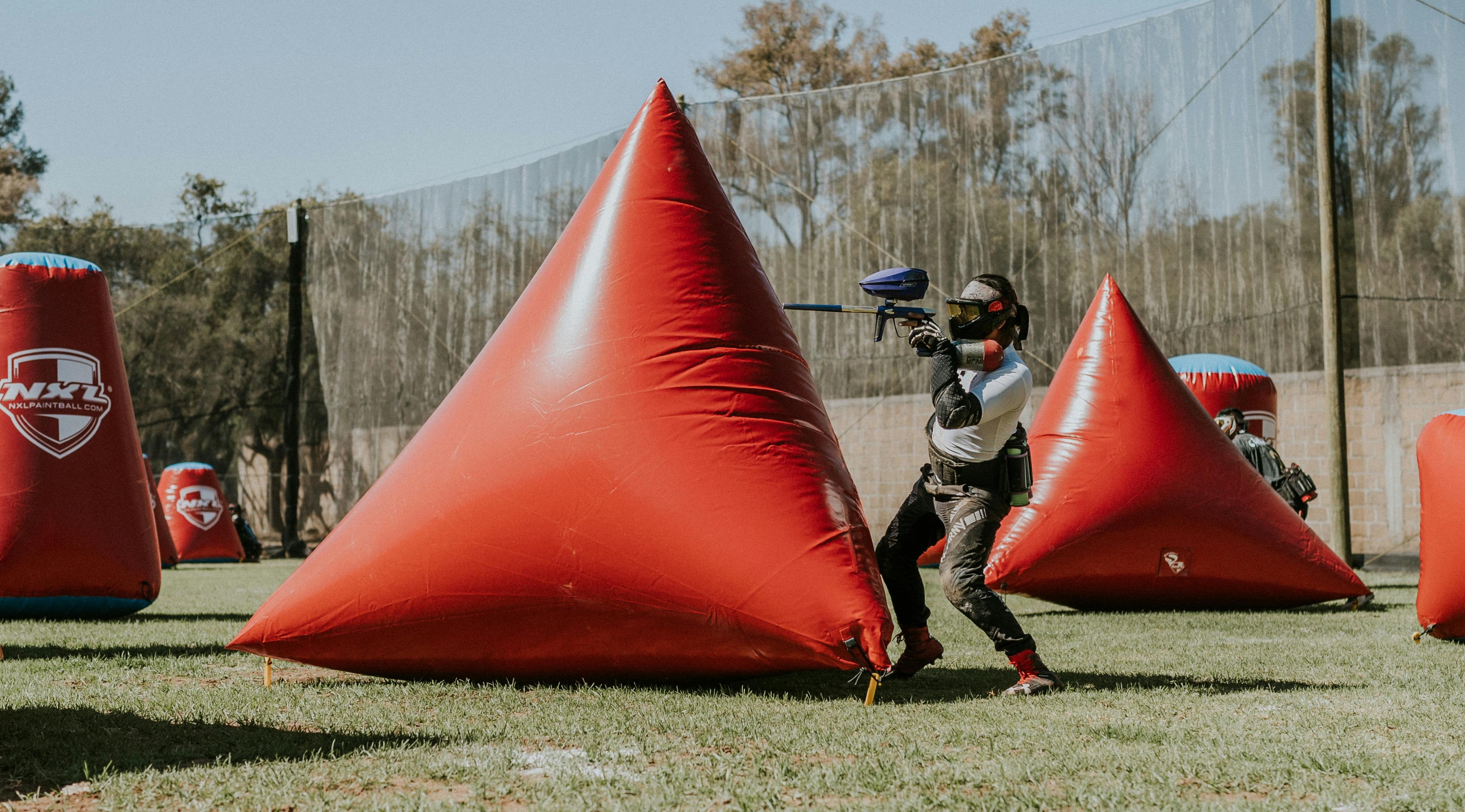Une femme joue au paintball en plein air avec un fusil au milieu de barrières gonflables. Prescription Goggle Inserts - A woman playing paintball outdoors using a rifle amid inflatable barriers.