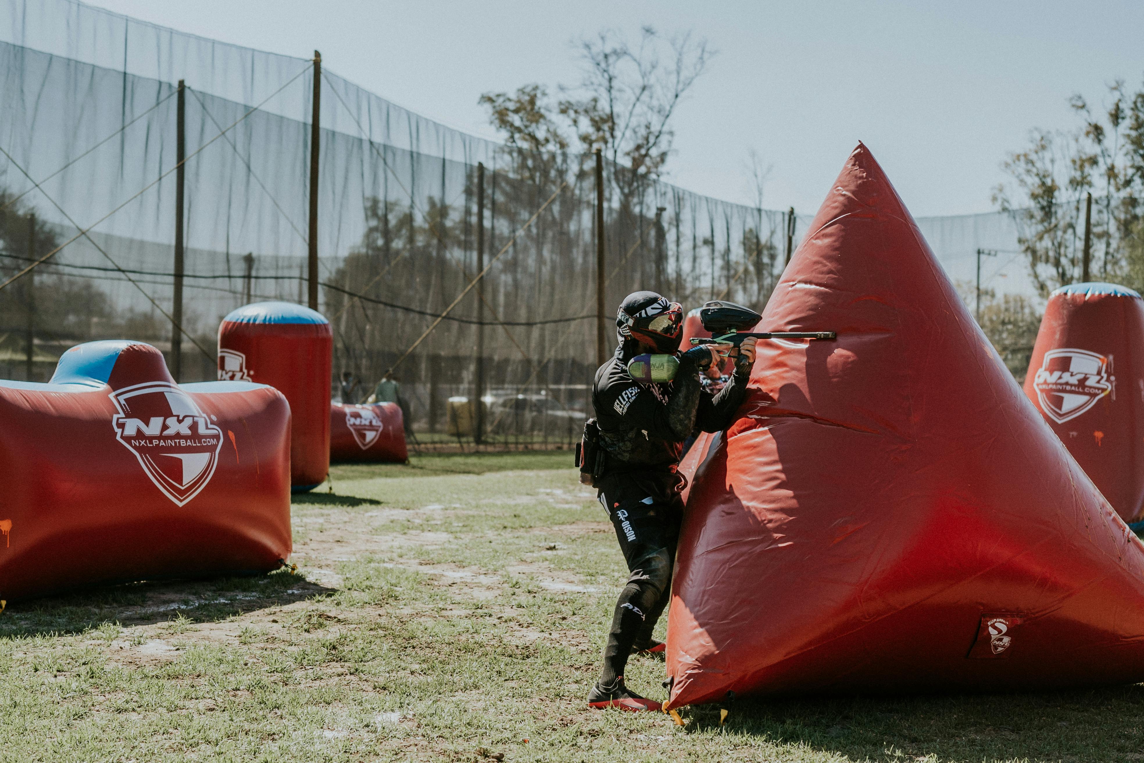 Un joueur de paintball élabore une stratégie derrière une couverture gonflable lors d'une compétition sur un terrain extérieur. Prescription Goggle Inserts - Paintball player strategizing behind inflatable cover during a competition on an outdoor field.