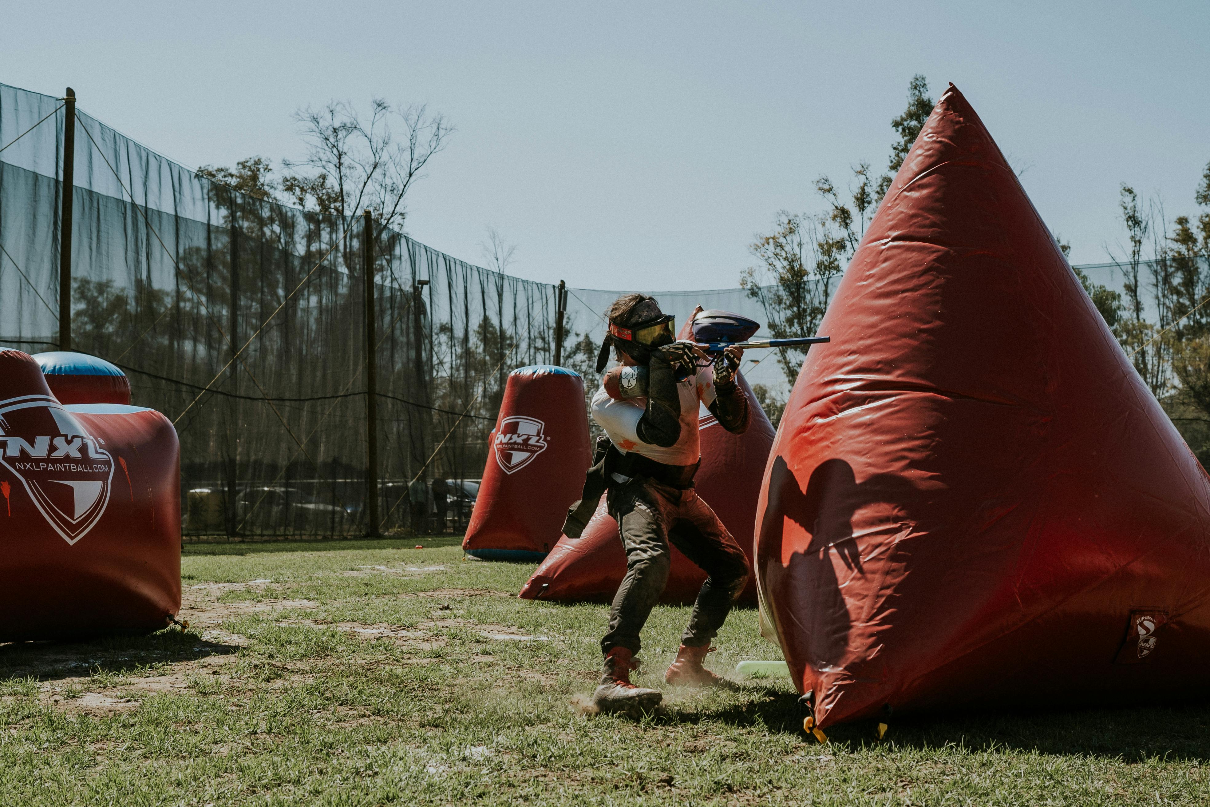 A person actively playing paintball outdoors, aiming behind inflatable covers. Prescription Goggle Inserts - A person actively playing paintball outdoors, aiming behind inflatable covers.