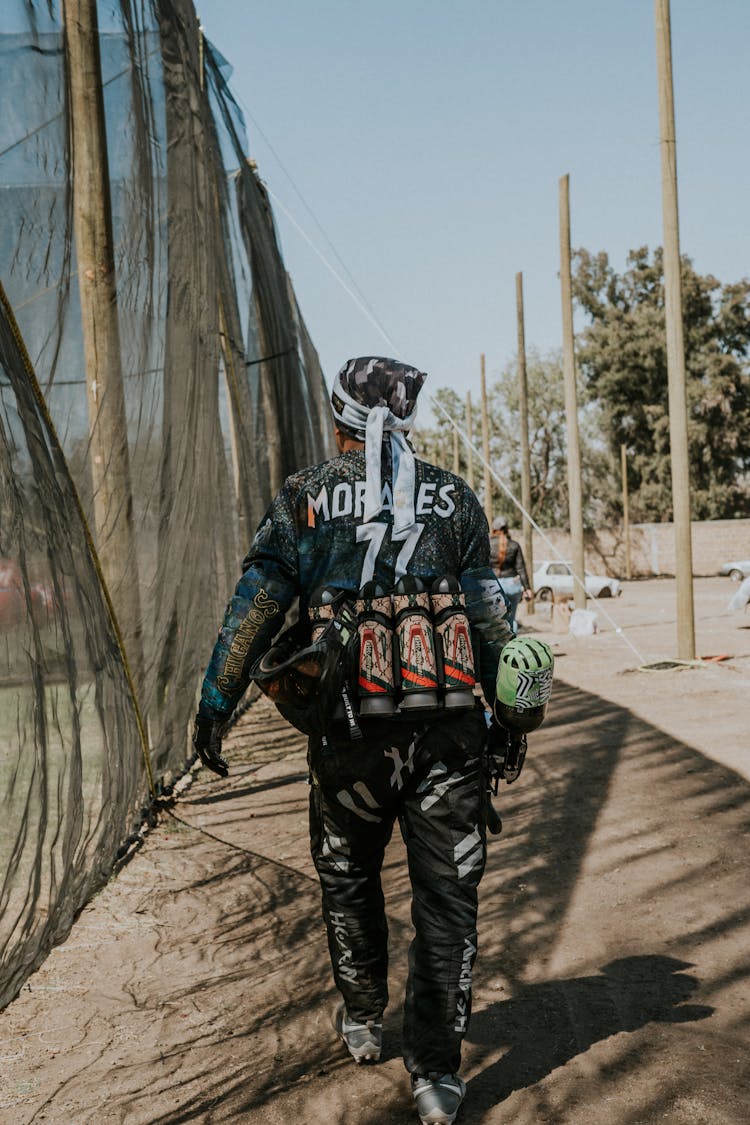 Back View Of A Man Walking With Paintball Equipment