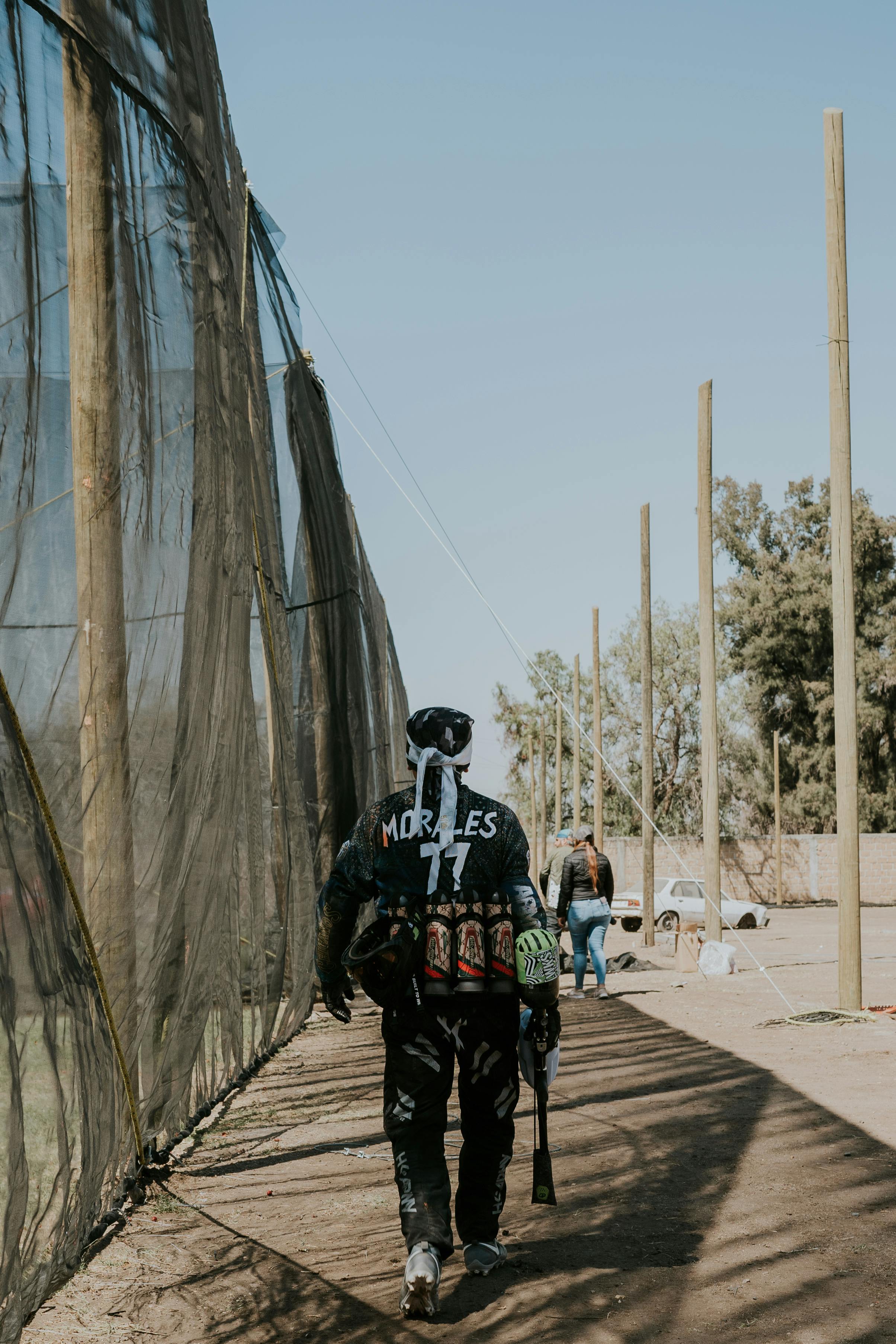 A paintball player in gear walking alongside a netted area on a sunny day. Prescription Goggle Inserts - A paintball player in gear walking alongside a netted area on a sunny day.
