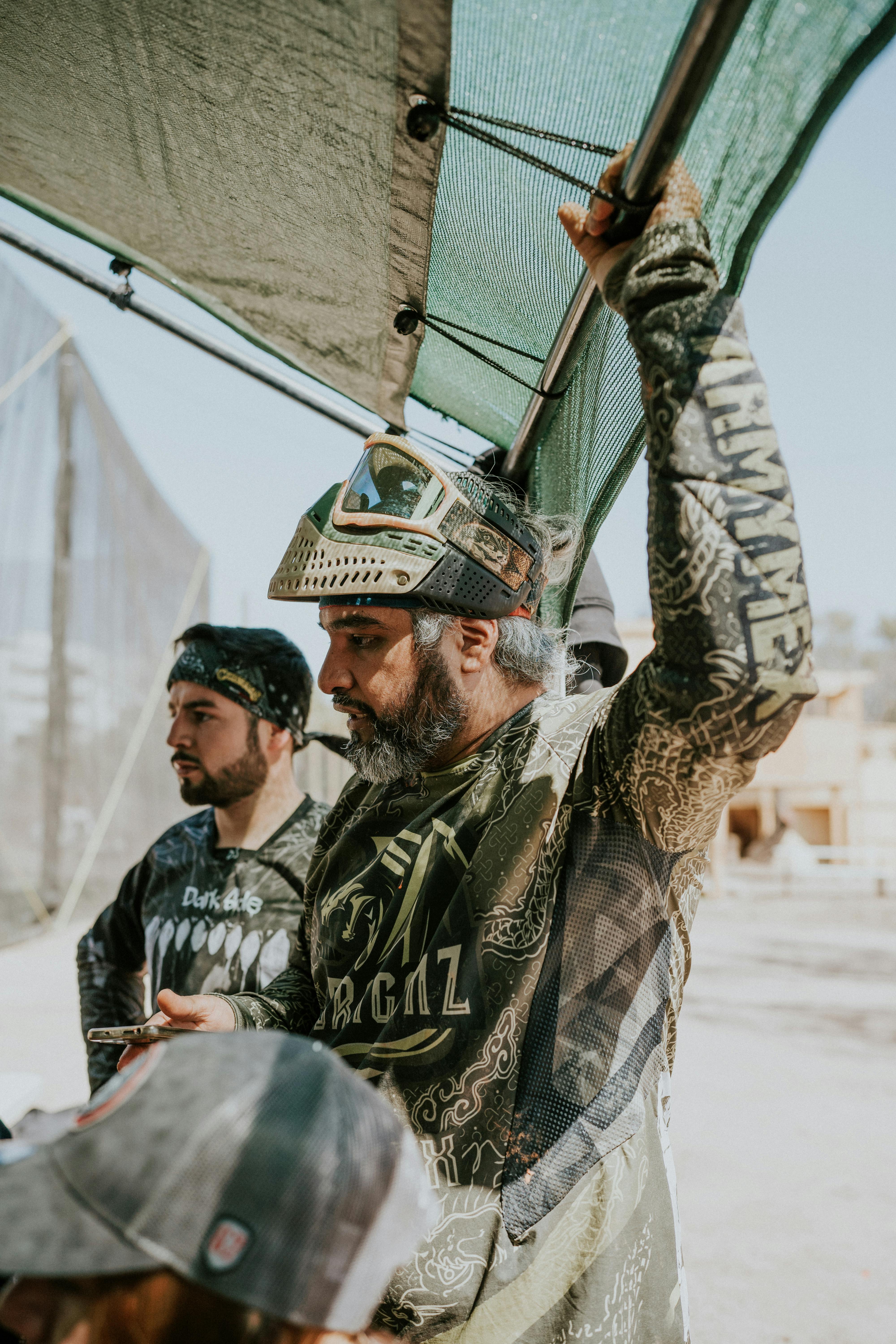 Two men in full paintball gear, wearing masks and standing under a canopy outdoors. Prescription Goggle Inserts - Two men in full paintball gear, wearing masks and standing under a canopy outdoors.