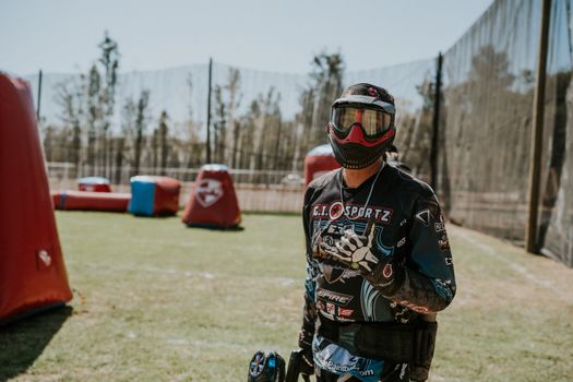 Paintball player in full gear and mask standing on an outdoor field ready for a match.