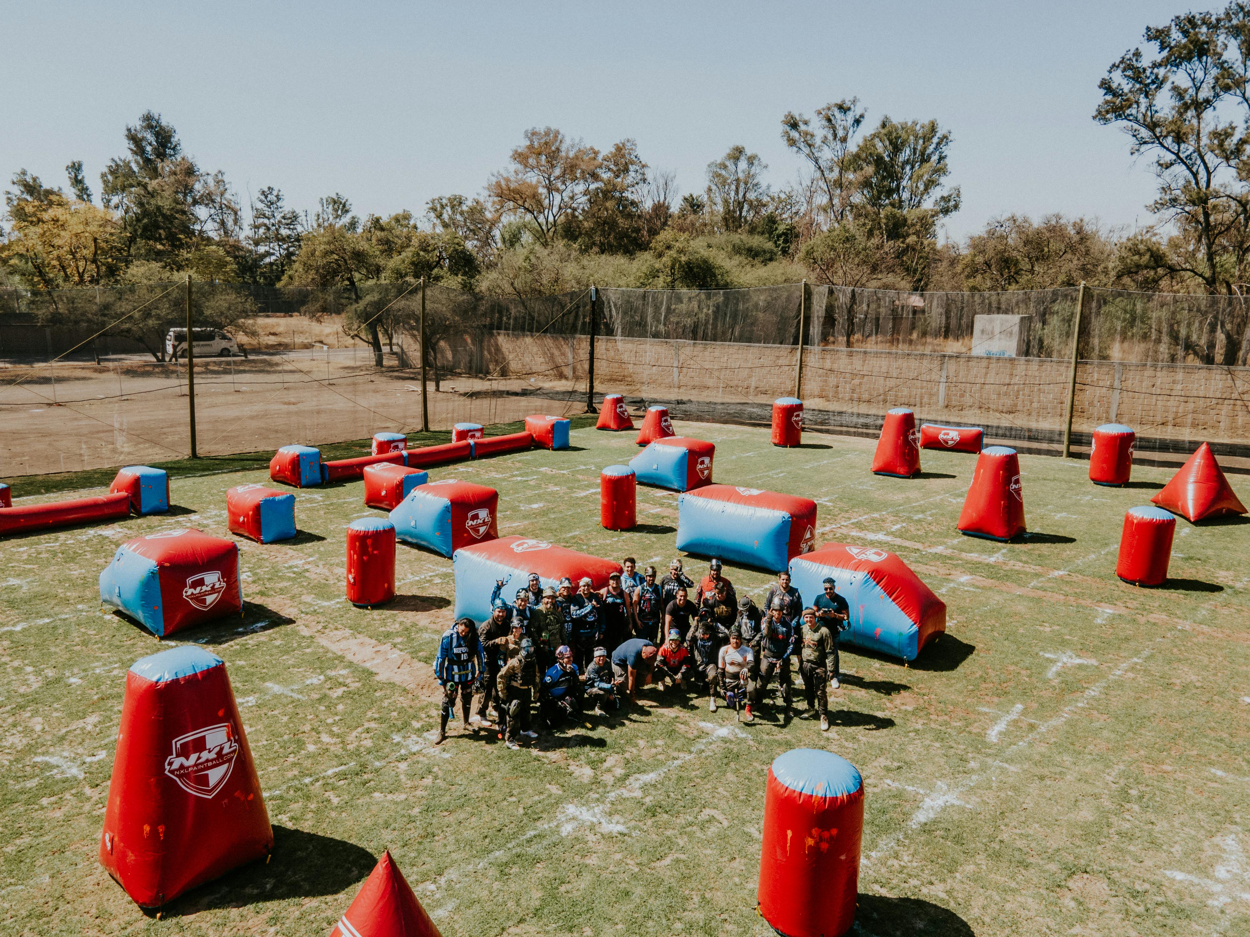Eine Luftaufnahme einer Gruppe von Menschen, die im Freien auf einem markierten Feld Paintball spielen. Prescription Goggle Inserts - An aerial view of a group of people playing paintball on a marked field outdoors.
