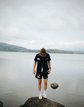 A stylish individual posing on rocks at a lakeshore, showcasing fashion and nature.