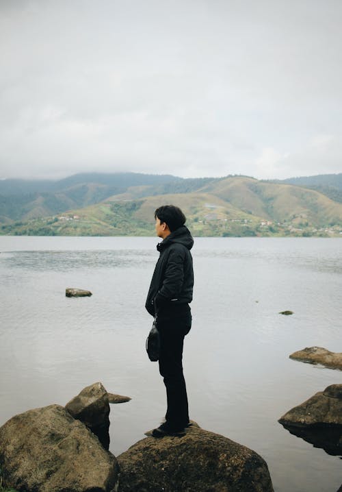 Man in Jacket Standing on Rocks on Sea Shore