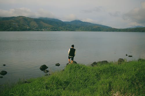 Man Standing on Rocks on Lakeshore