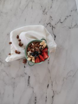 Overhead view of a fresh fruit and nut bowl on a marble surface with a napkin.
