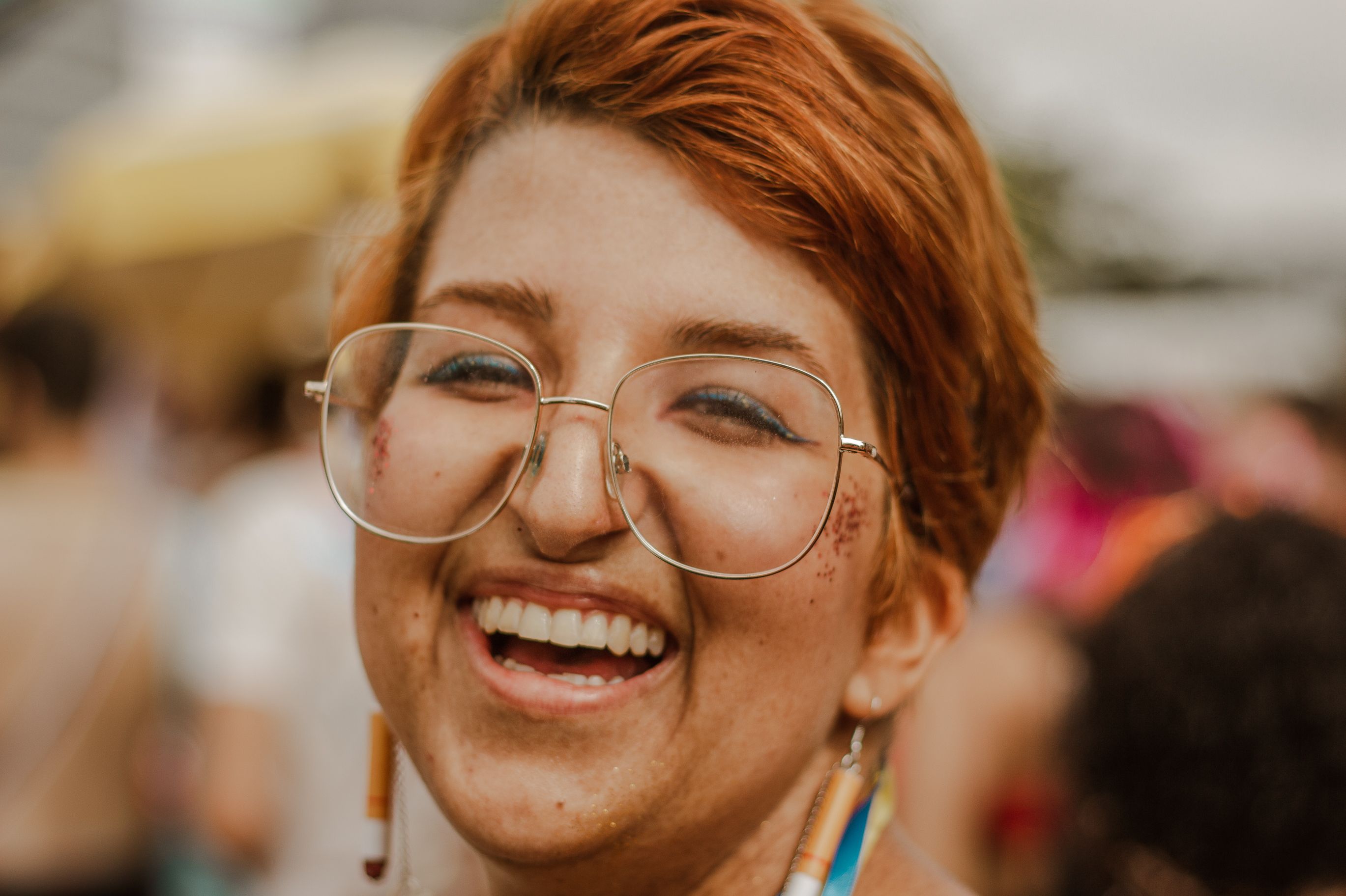 Close-up of a smiling woman with glasses enjoying a sunny day outdoors.