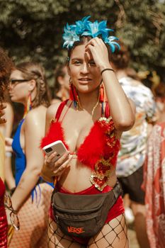 Vibrant carnival scene with a woman in a feathered costume holding a smartphone, enjoying the festivities.