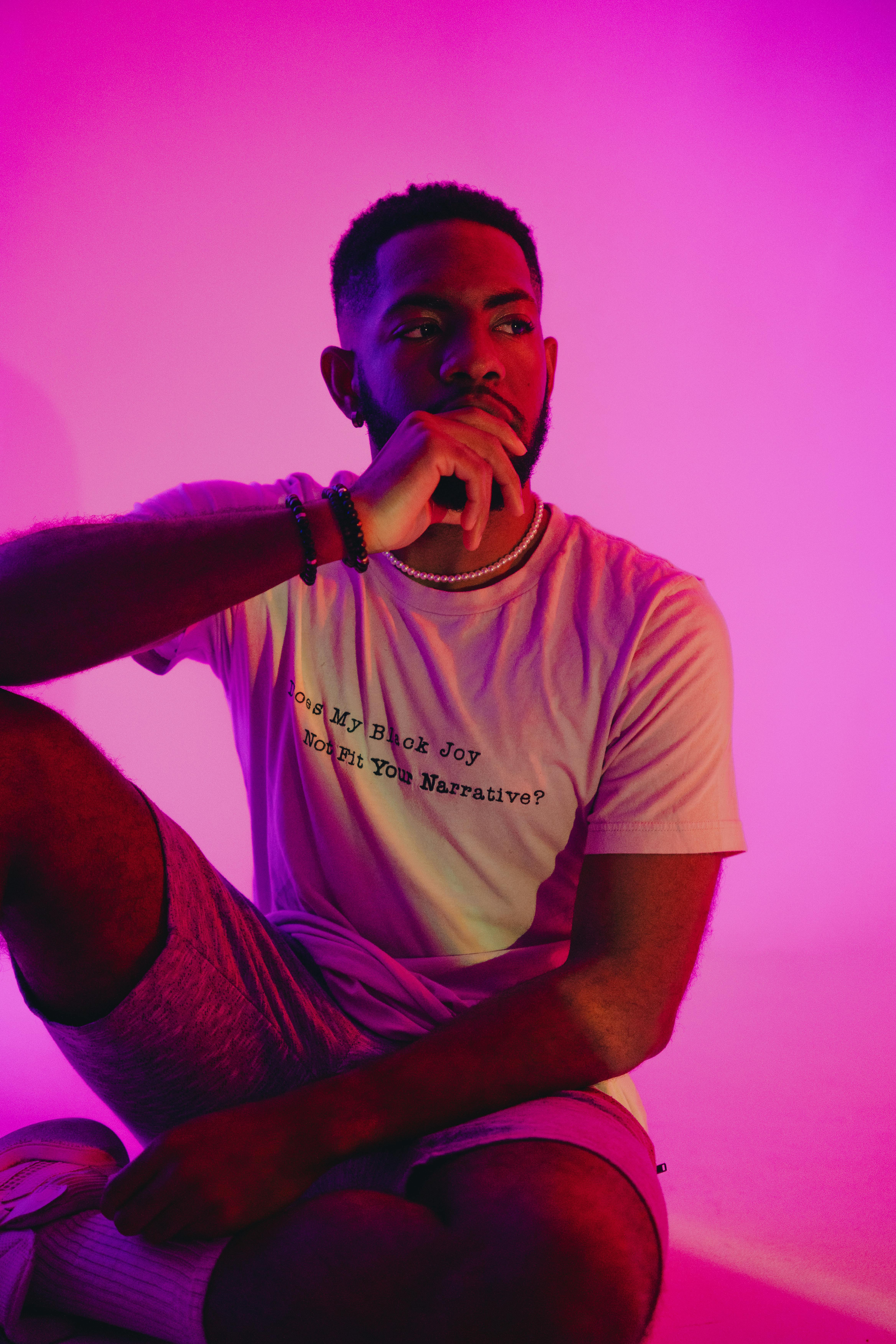 Stylish man in vibrant lighting, wearing a message t-shirt and engaging pose.
