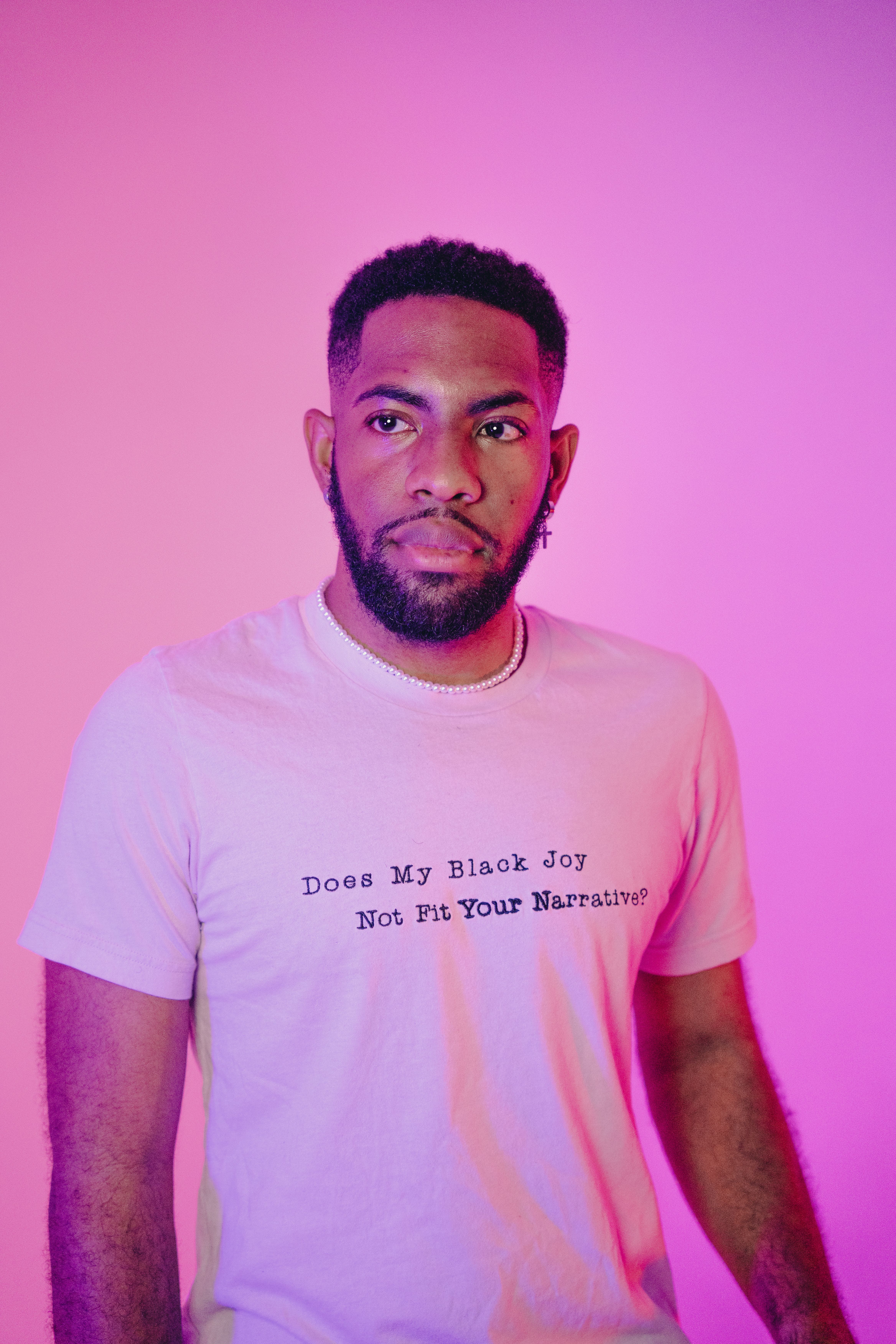 Portrait of a fashionable man in a pink-lit studio setting wearing a message t-shirt.