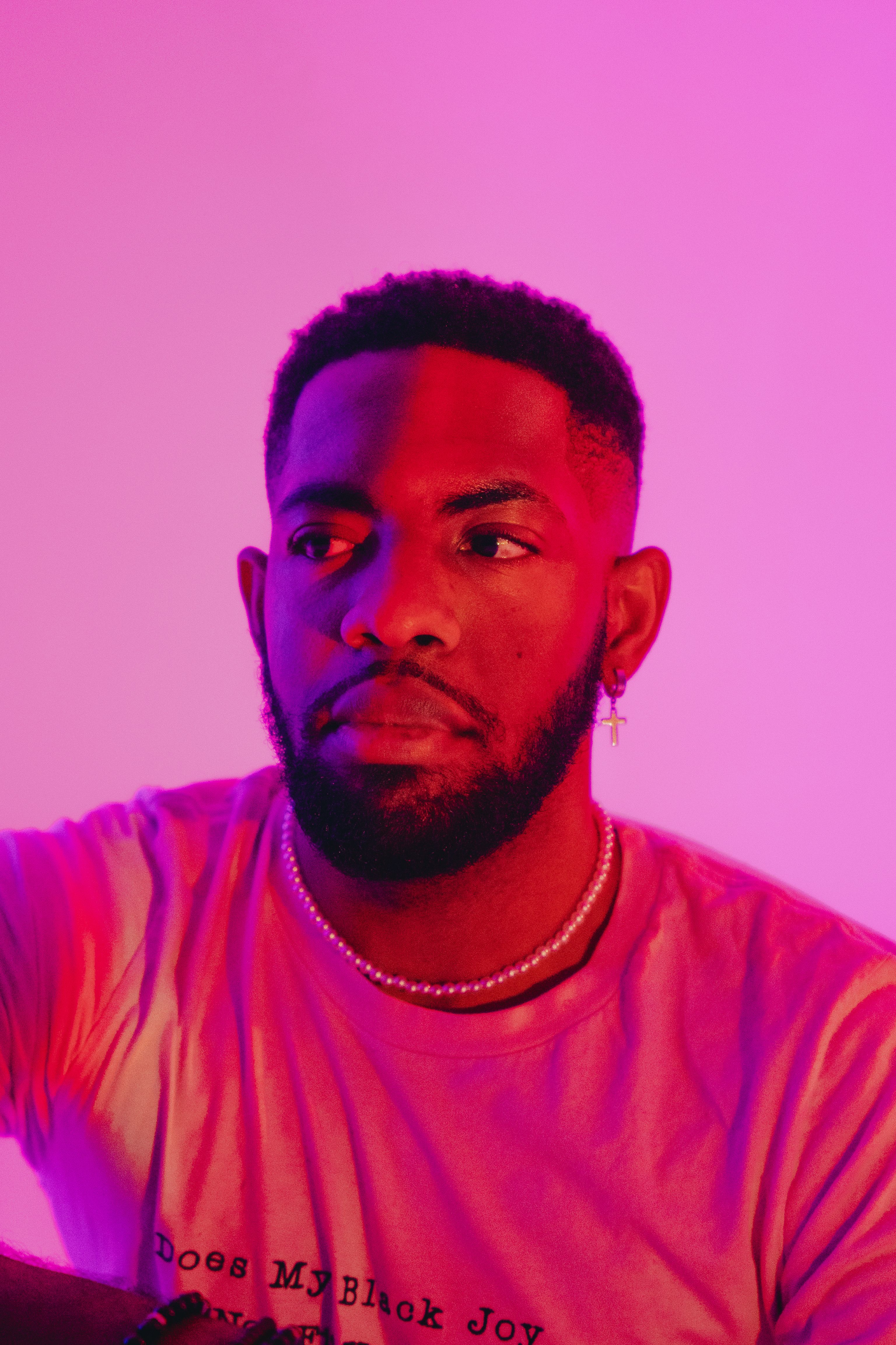 Portrait of a man with beard and pearl necklace bathed in vivid pink light.