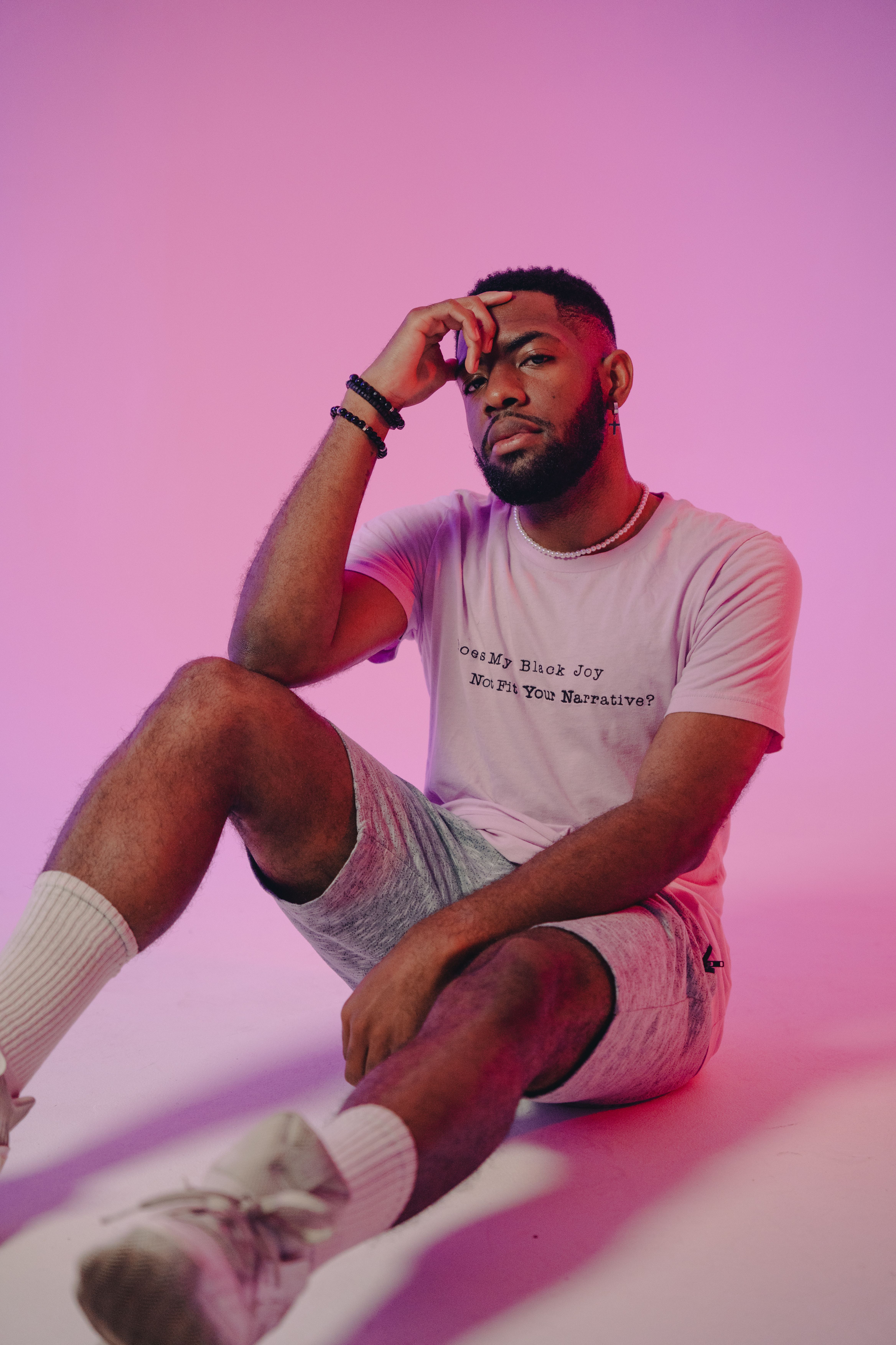 Young man poses stylishly against a vibrant pink gradient background, wearing a casual t-shirt and shorts.