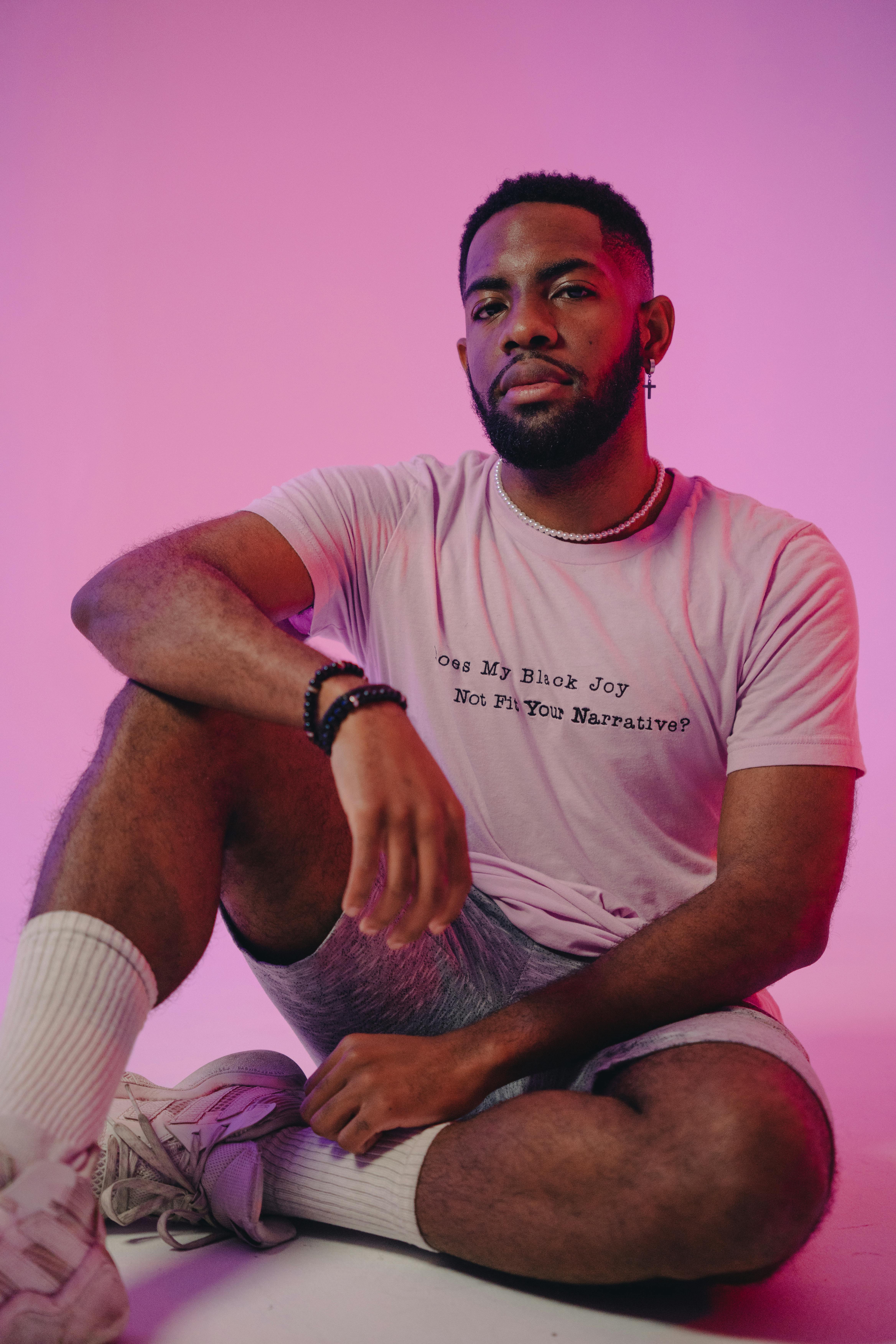 Young African American man sitting confidently in a modern studio setting with a pink background.