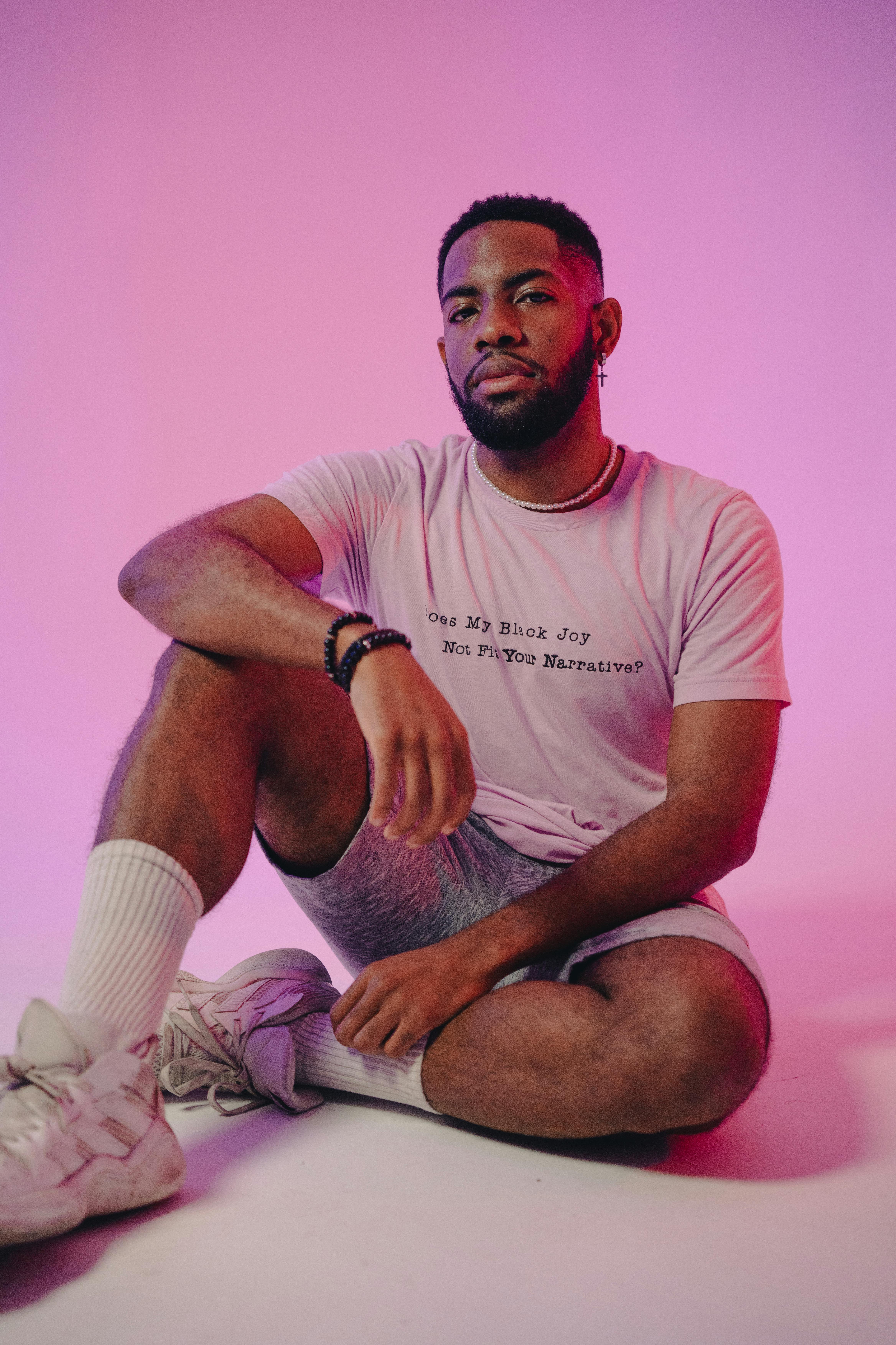 A fashionable man poses confidently against a vibrant pink backdrop.
