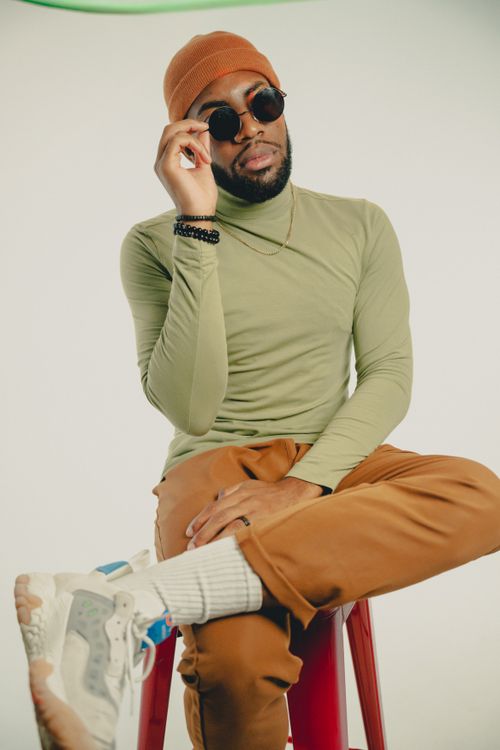 Free Stylish man in sunglasses and beanie posing on a stool with a chic urban vibe. Stock Photo