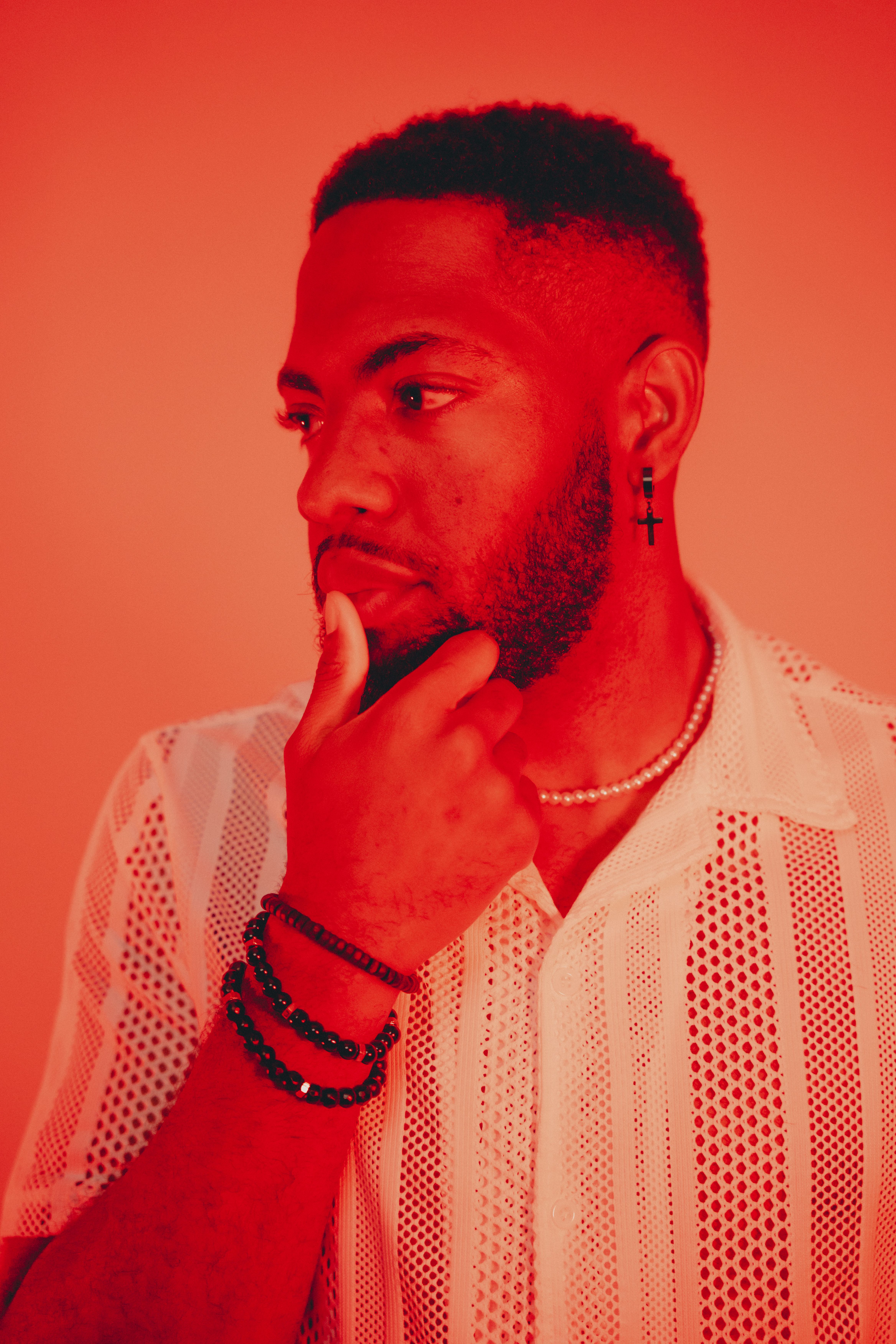 Profile portrait of thoughtful man with beaded bracelet and earring under red lighting.
