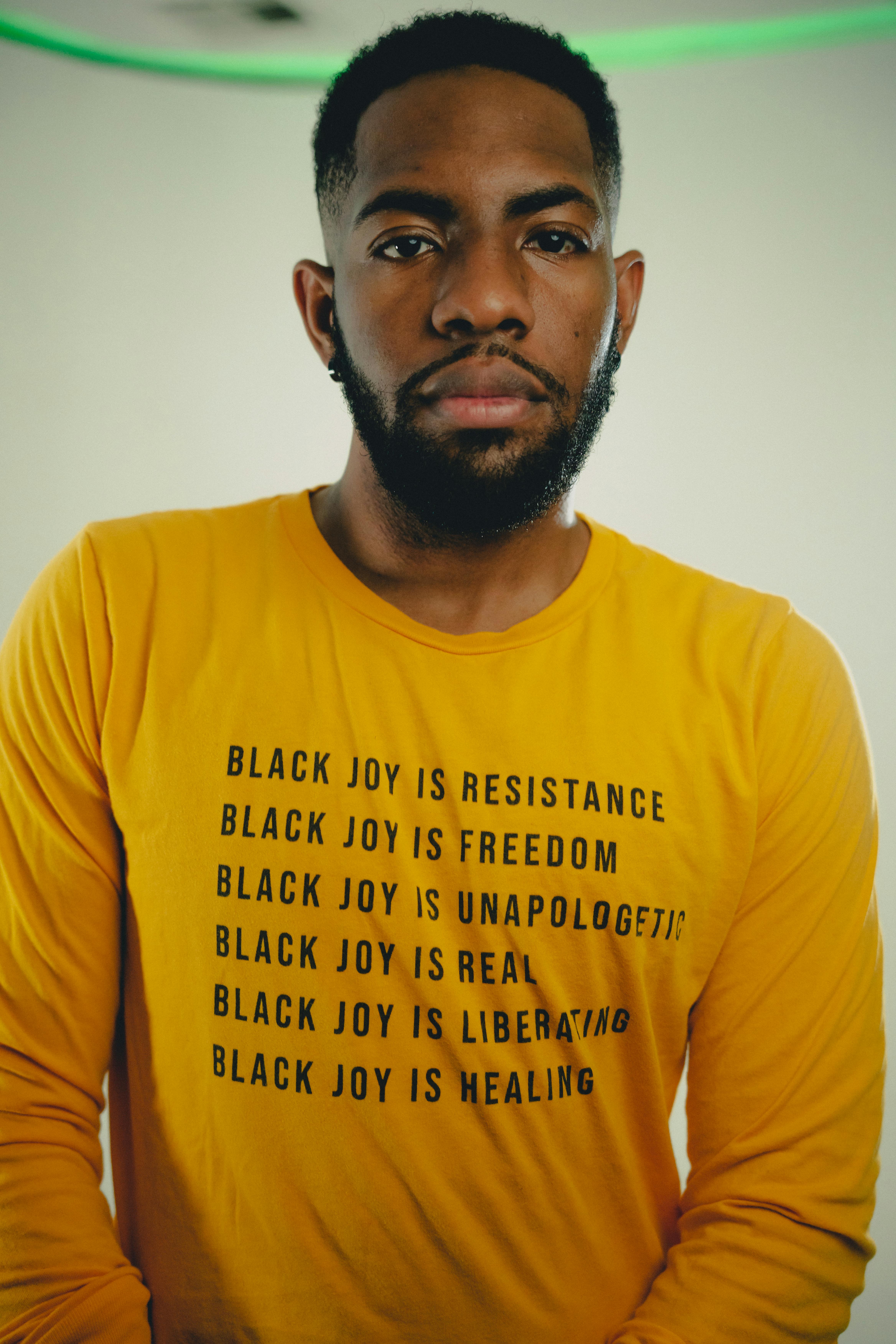 A striking portrait of a man wearing a yellow shirt with empowering text promoting black joy and freedom.