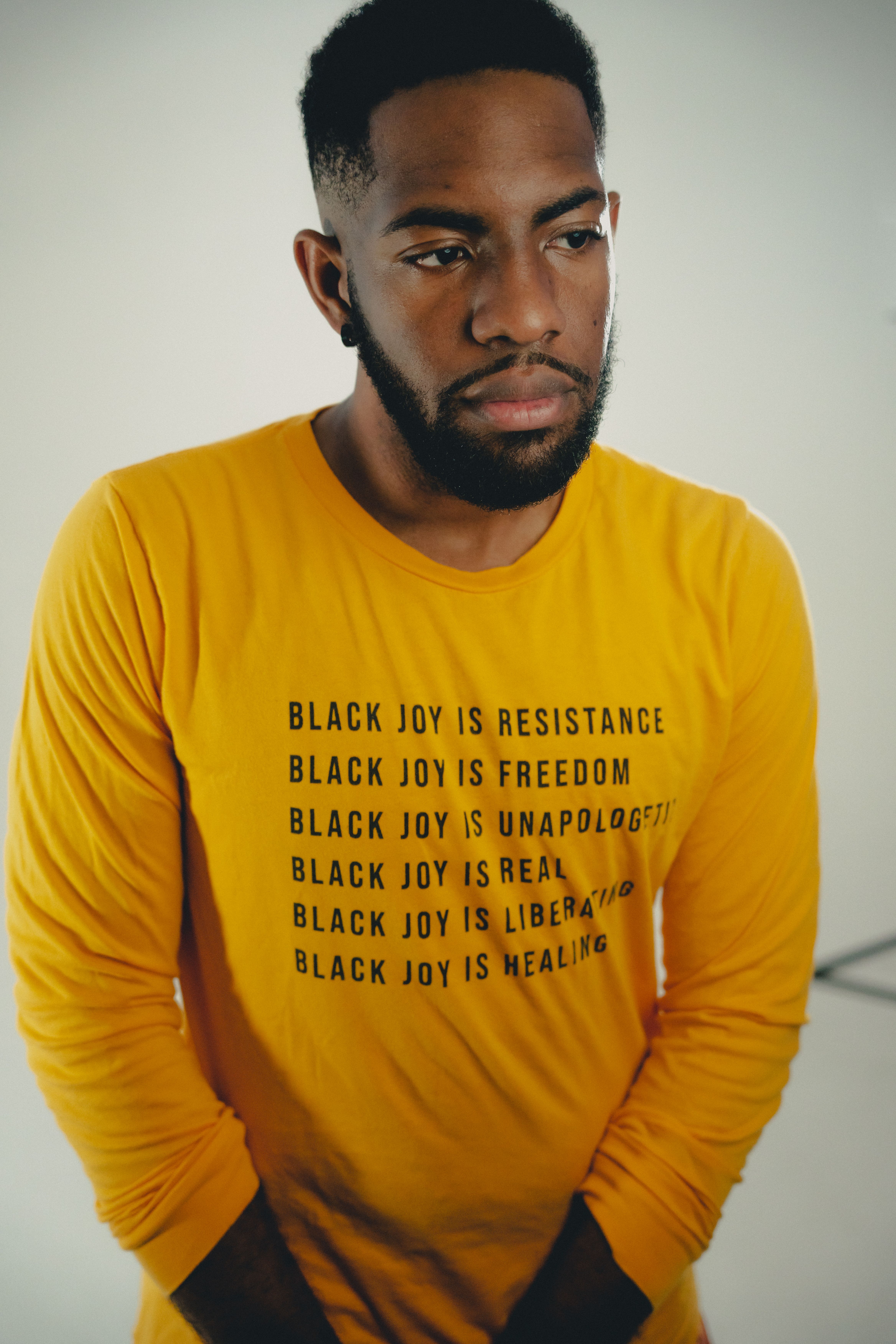 Man in yellow shirt with 'Black Joy' messages, studio portrait.