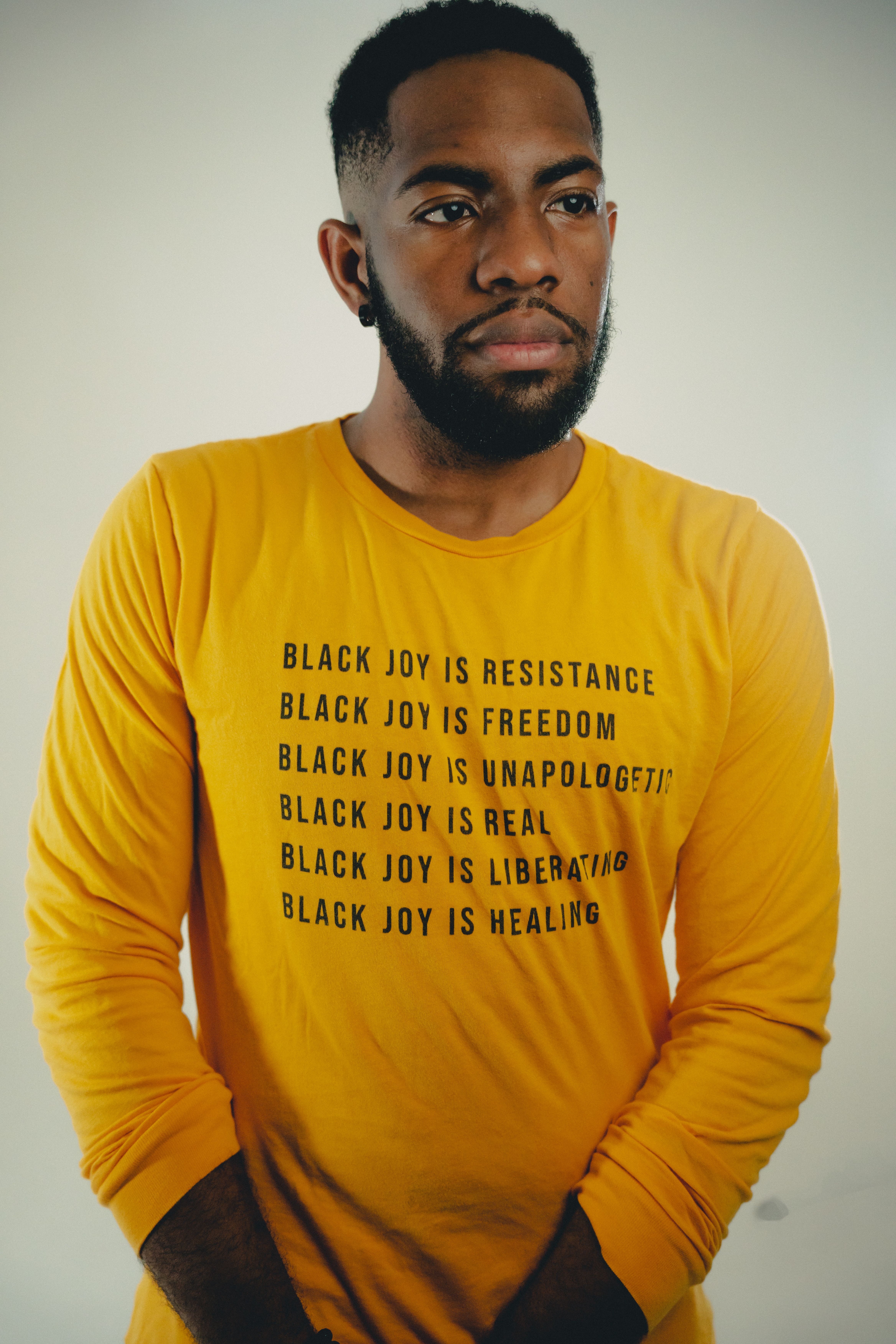 A powerful portrait of a man wearing a yellow shirt with an inspiring message about black joy.
