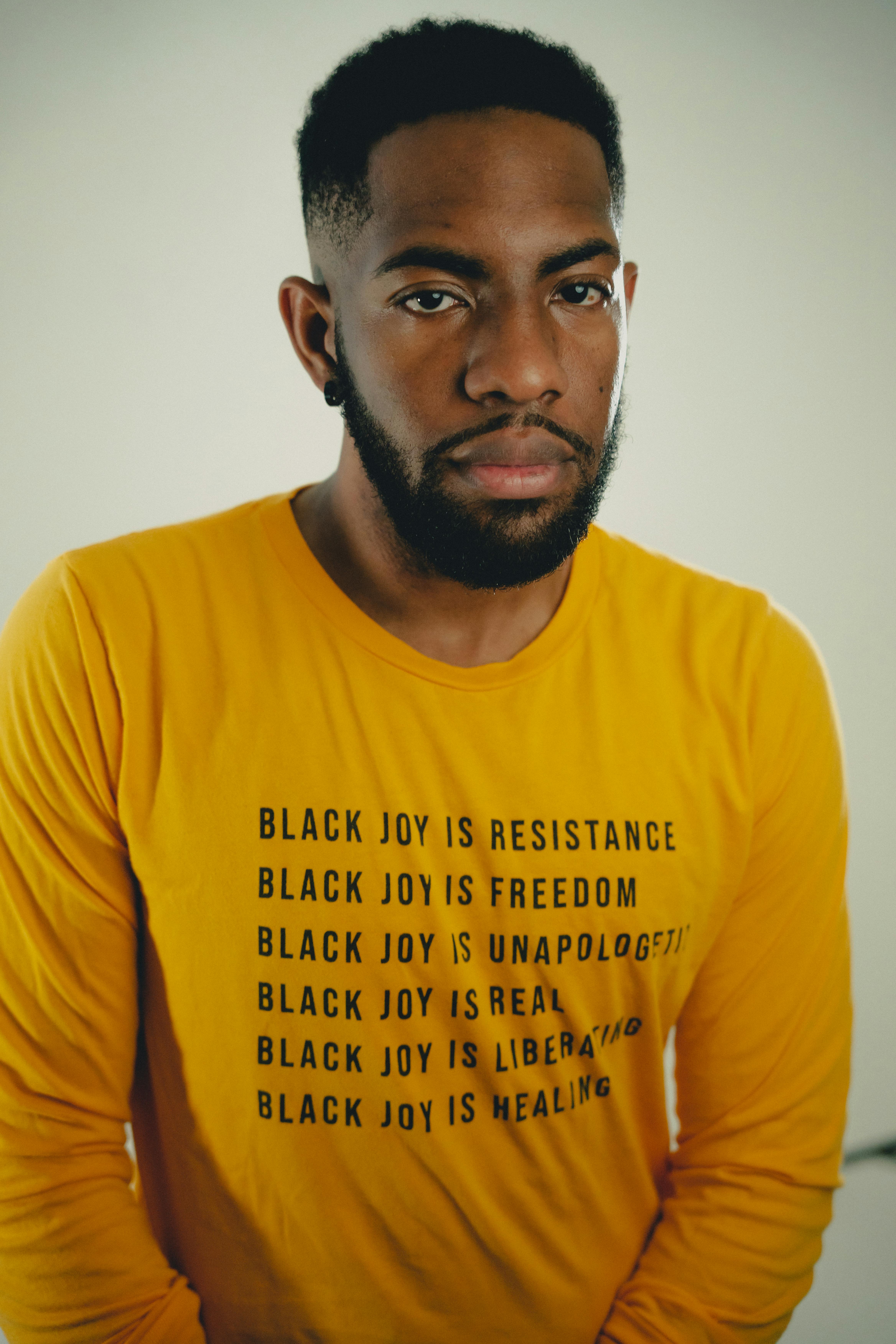 Portrait of a stylish young man wearing a yellow shirt with inspiring text promoting Black joy and resistance.